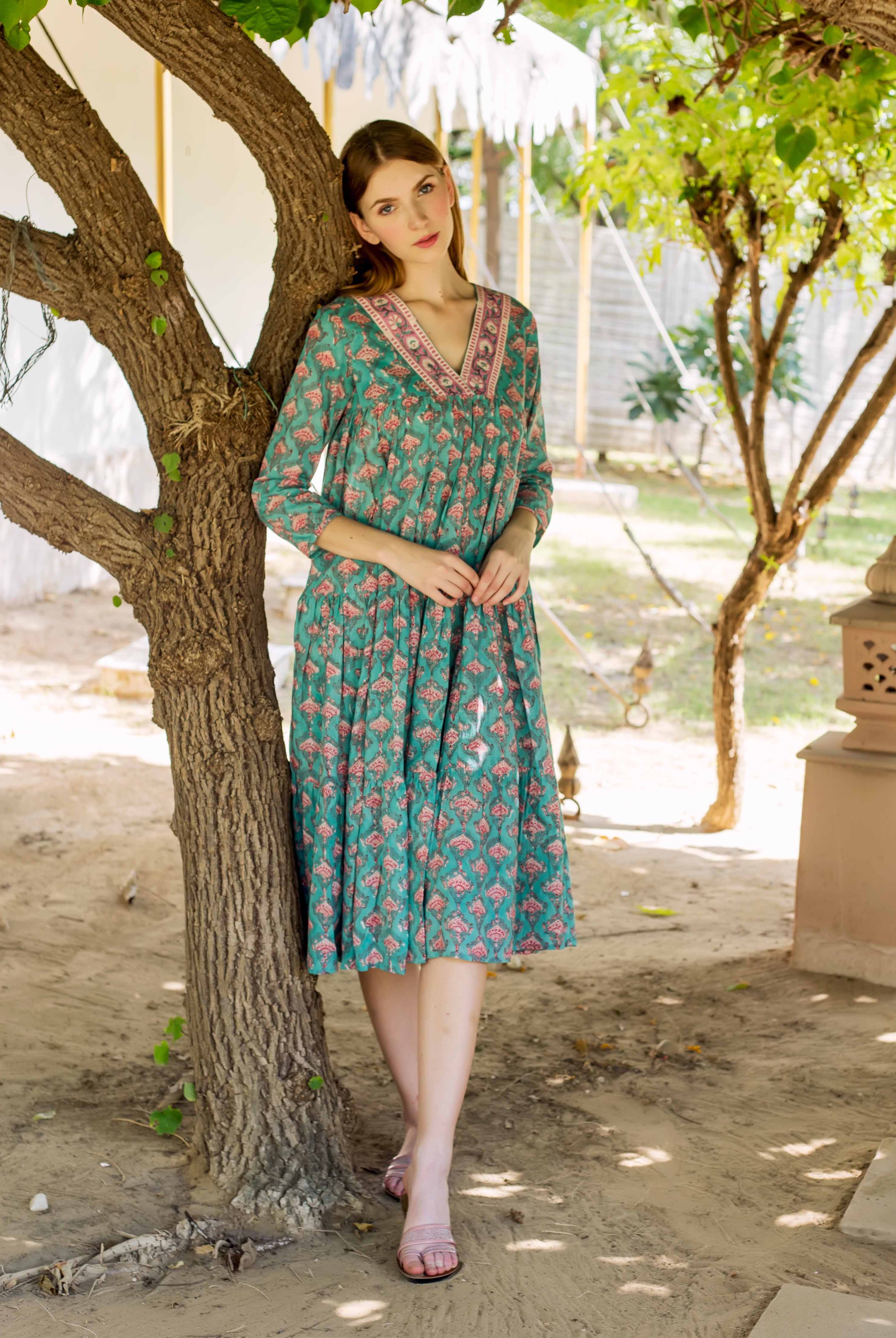 Model wearing a teal green V-neck tiered dress with a pink block print.