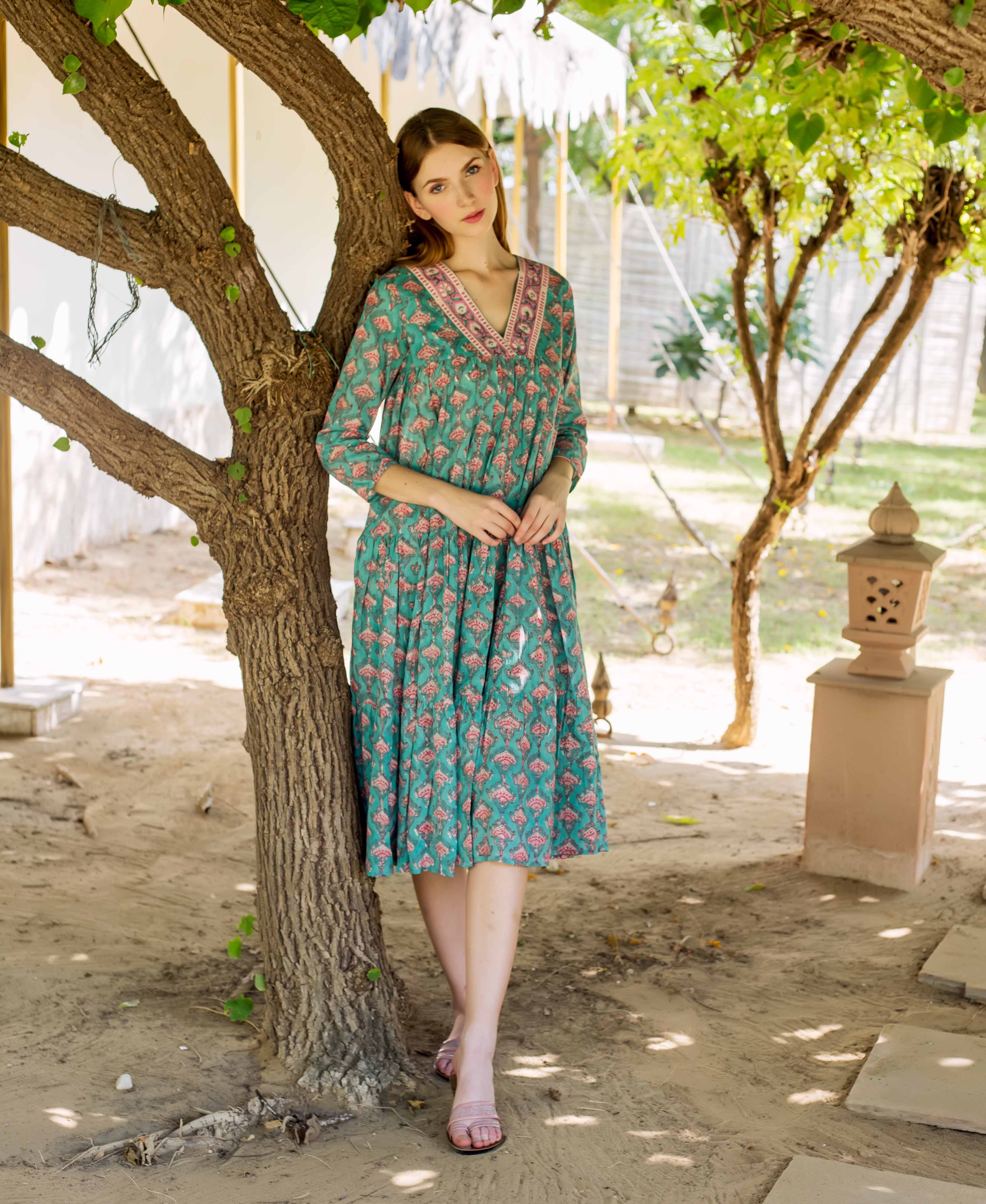 Model wearing a teal green V-neck tiered dress with a pink block print.