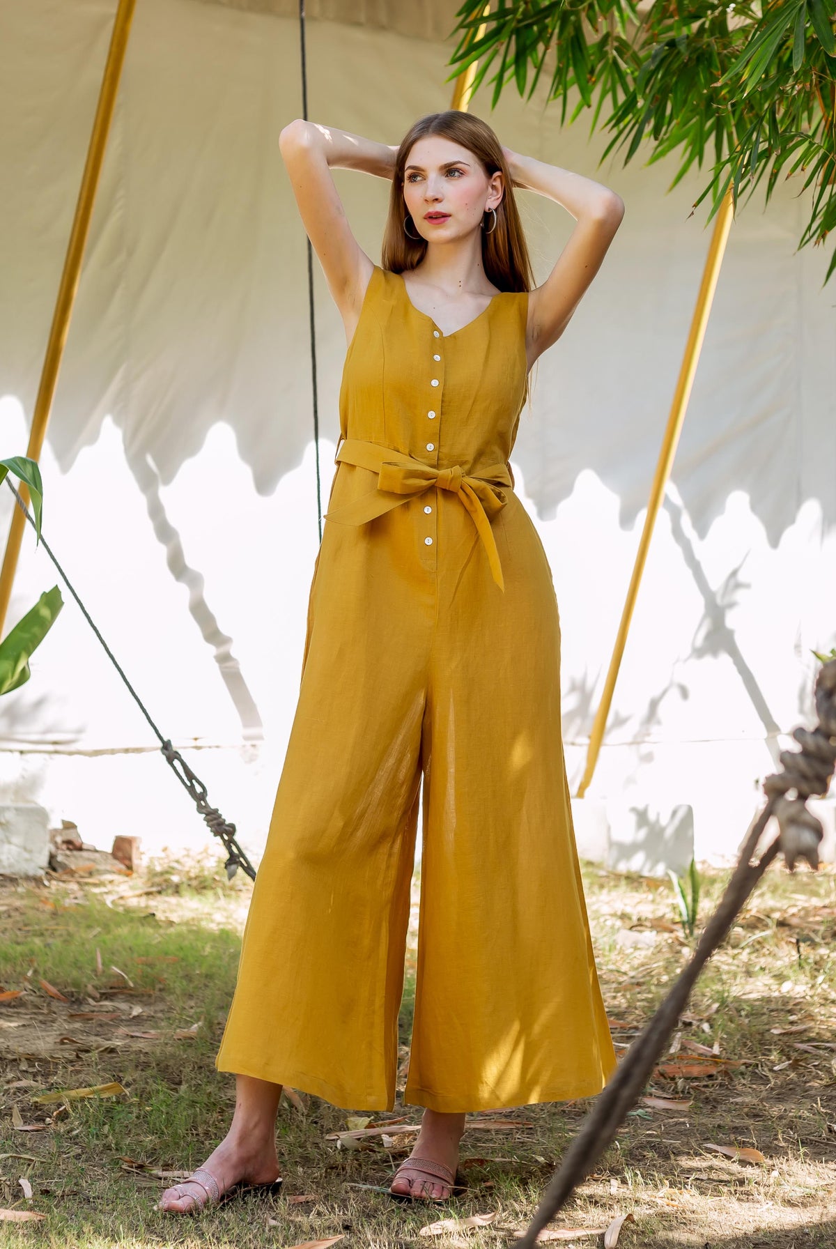 Full body, front view of a model wearing an ochre sleeveless button-front tie-waist wide-leg jumpsuit.