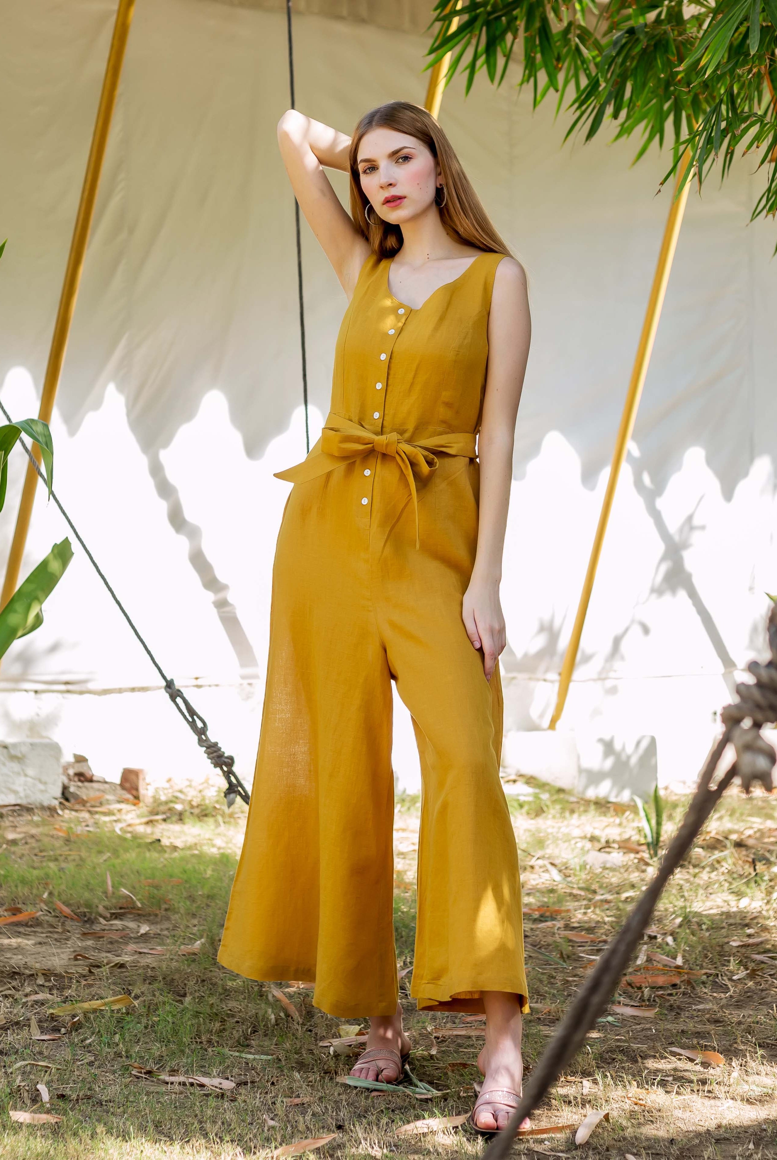 Female model in an ochre sleeveless button-front tie-waist wide-leg jumpsuit.