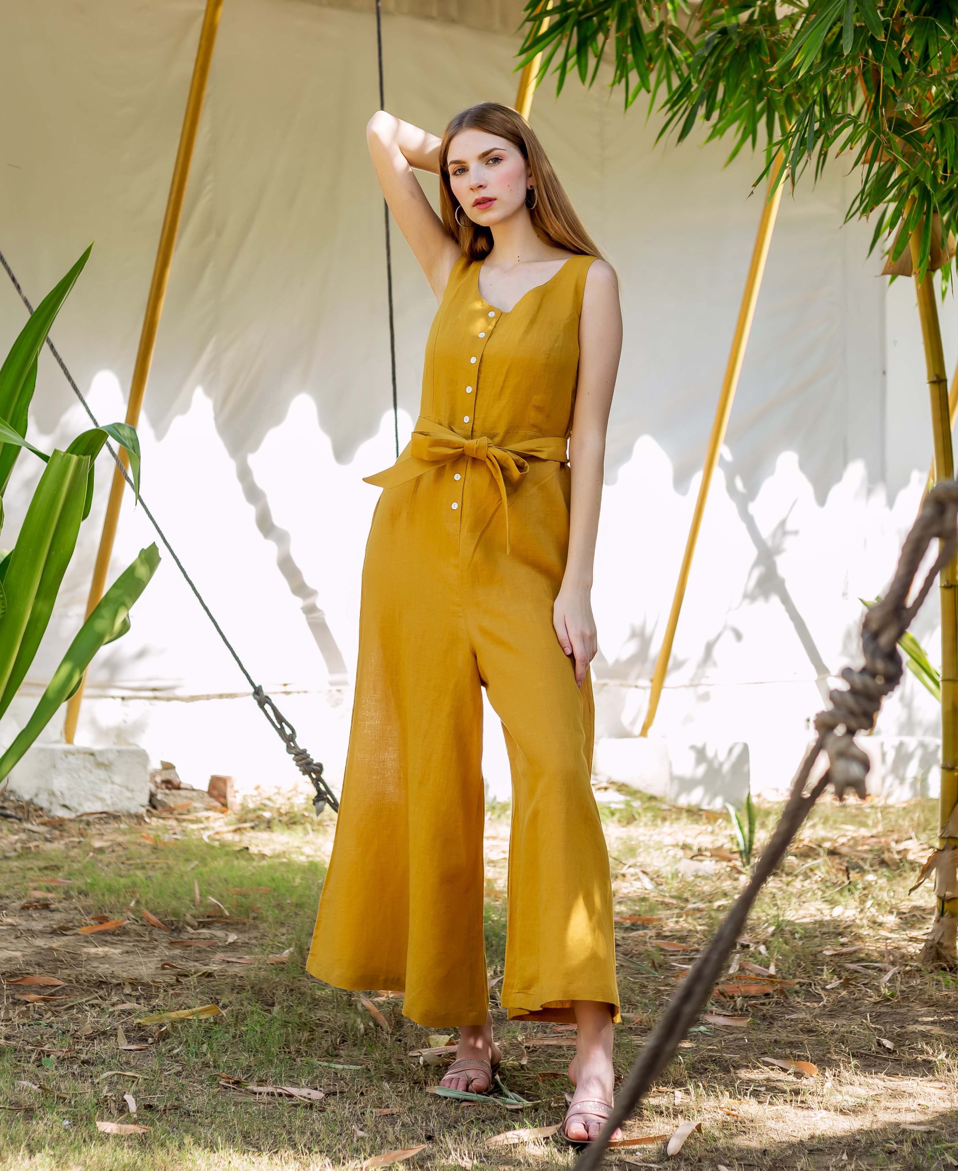 Female model in an ochre sleeveless button-front tie-waist wide-leg jumpsuit.