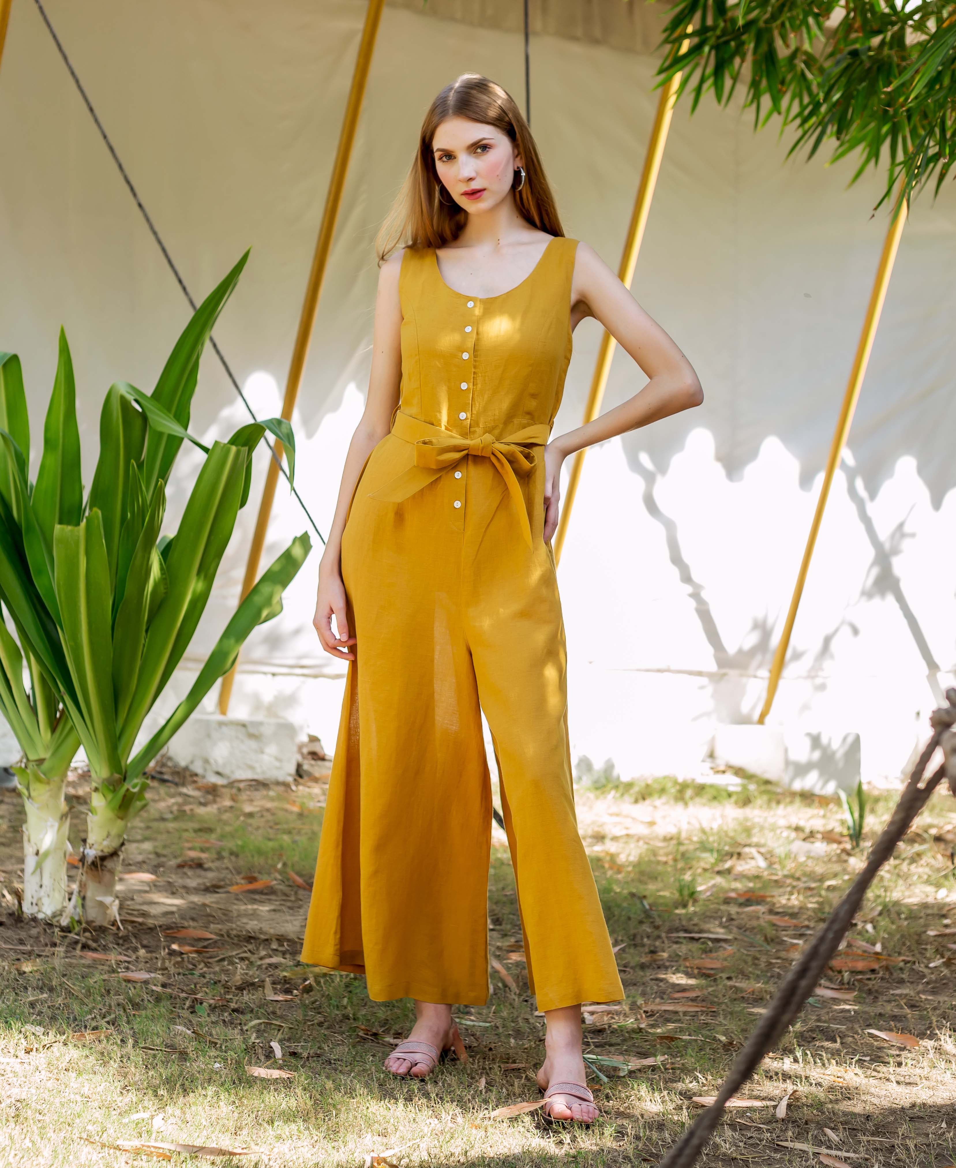 Woman in an ochre sleeveless jumpsuit with button front, tie-waist, and wide legs.