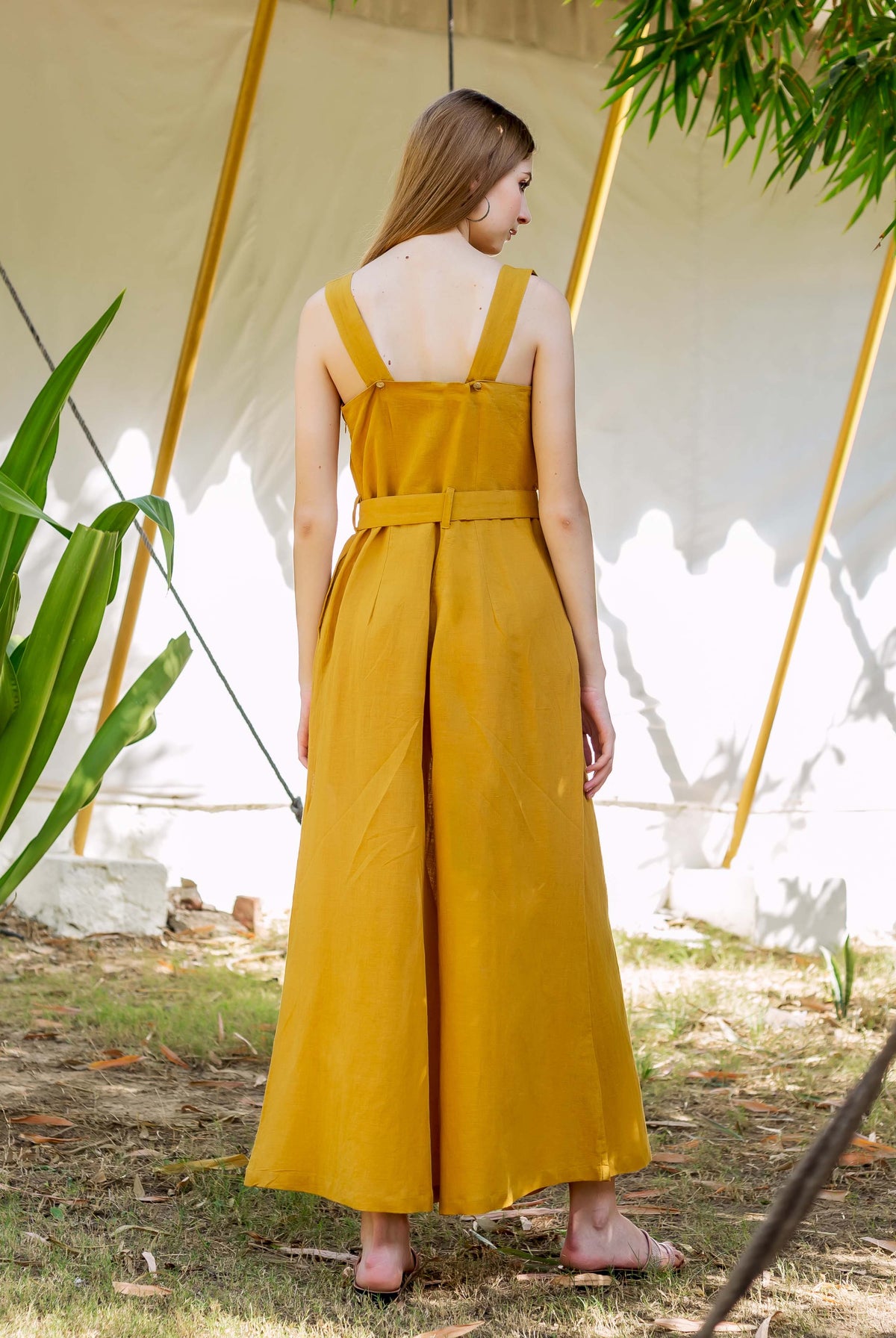Model from behind wears an ochre belted sleeveless jumpsuit with wide legs.
