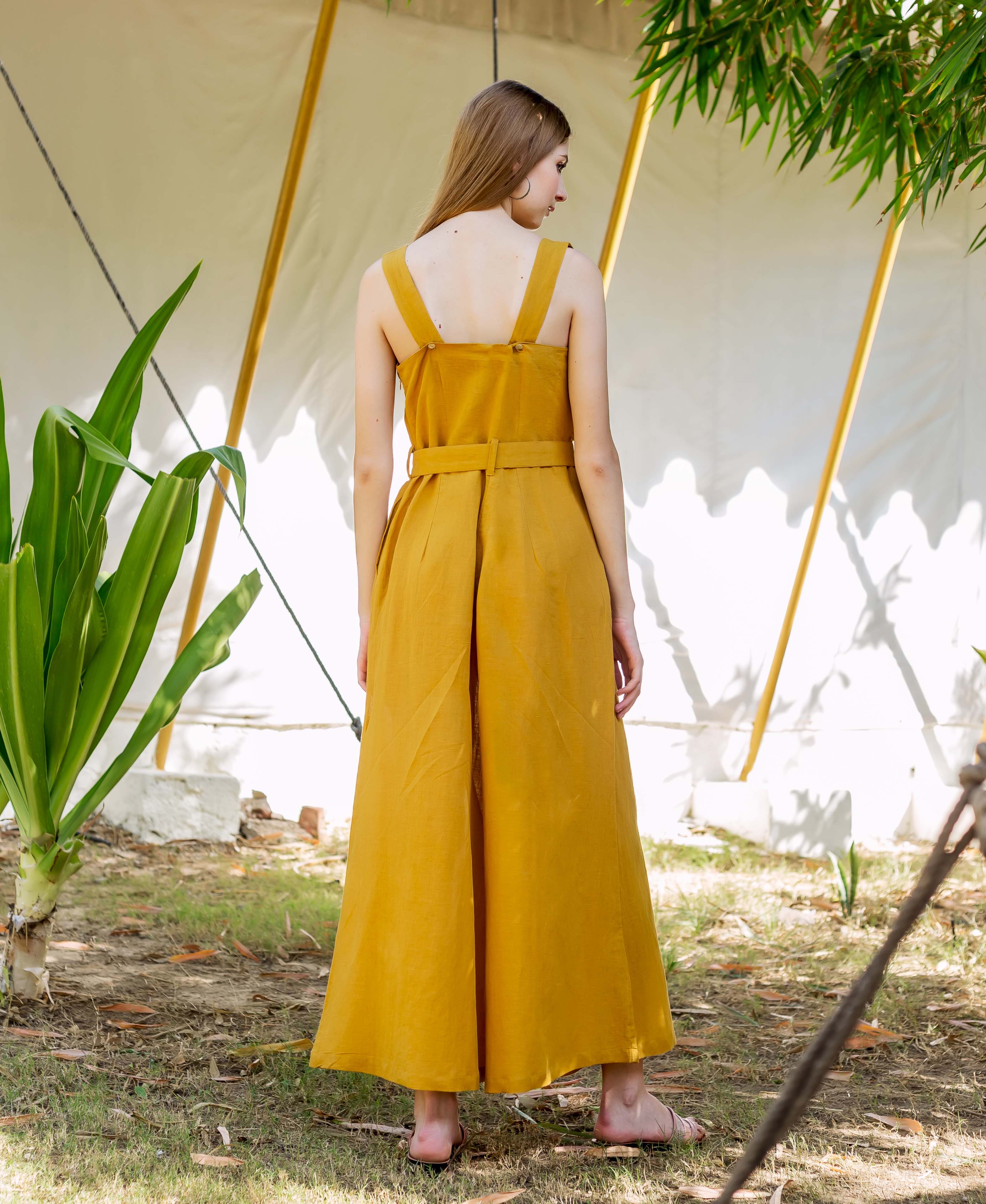 Model from behind wears an ochre belted sleeveless jumpsuit with wide legs.