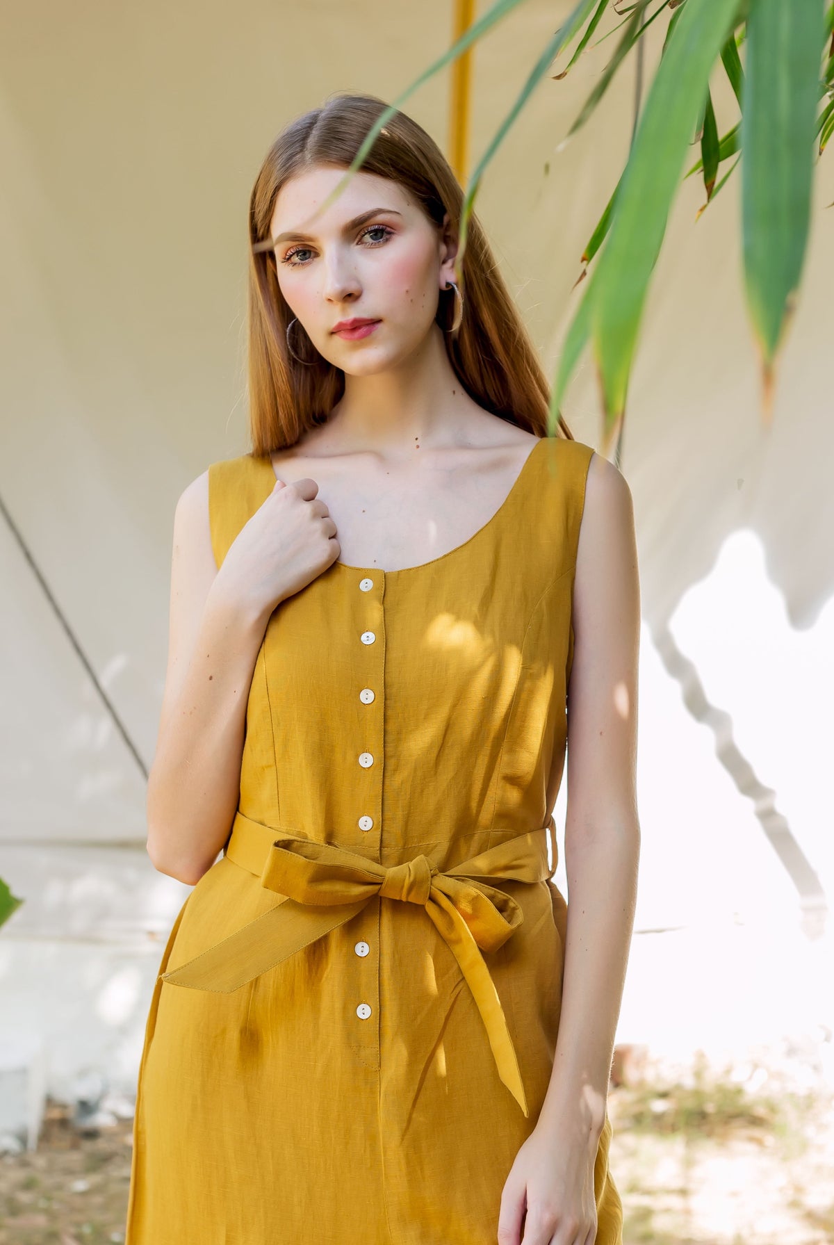 Model in an ochre sleeveless button-down dress with a self-tie waist belt.