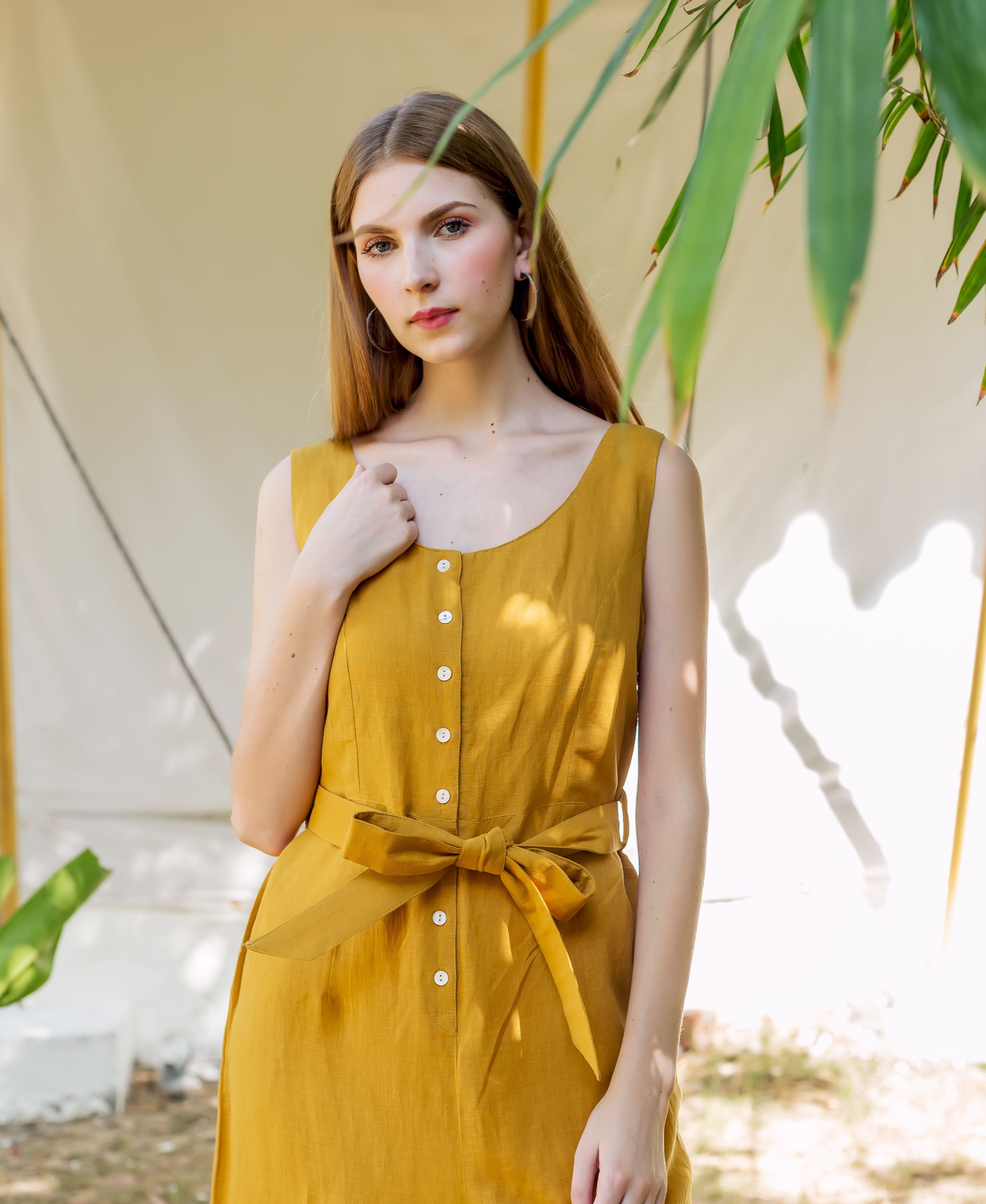 Model in an ochre sleeveless button-down dress with a self-tie waist belt.