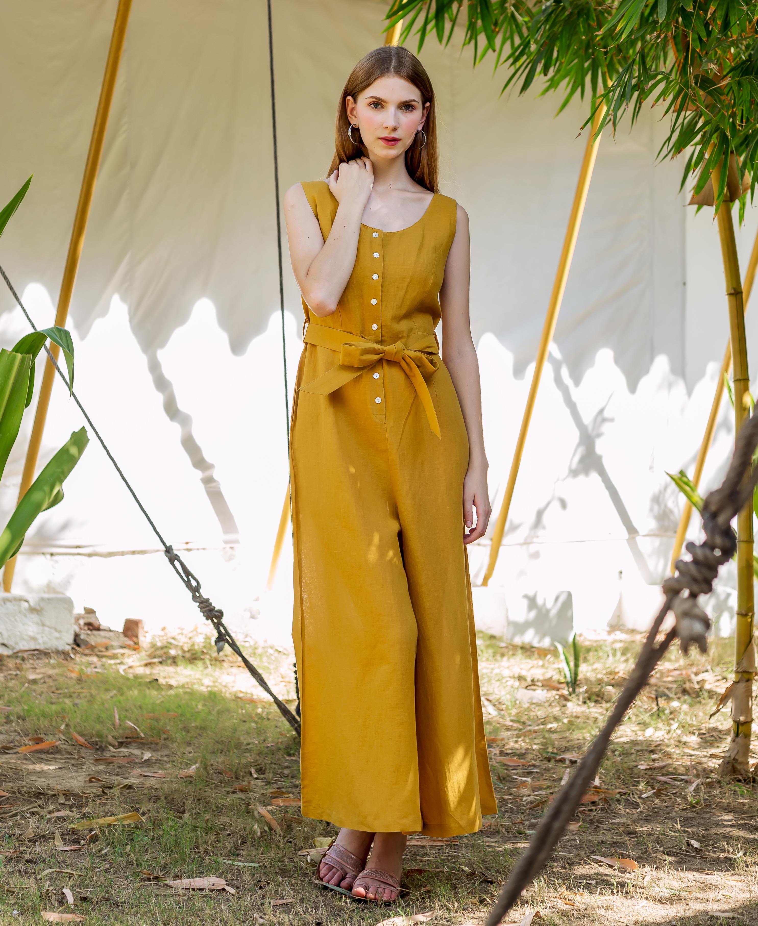 Woman in a sleeveless ochre button-down jumpsuit with a tied waist, standing outdoors.