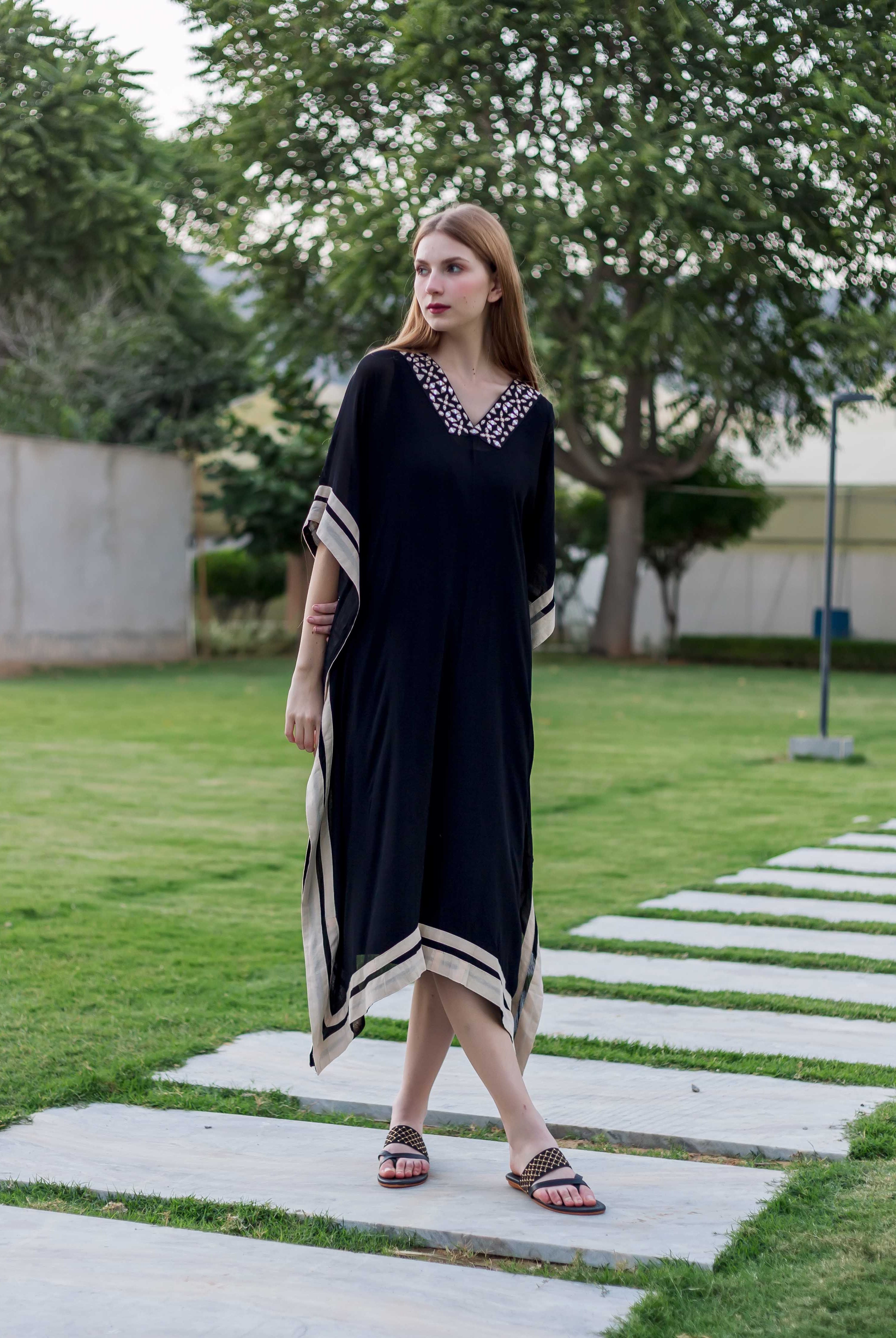 Model in front view wearing black kaftan with white embroidered V-neck and striped borders.