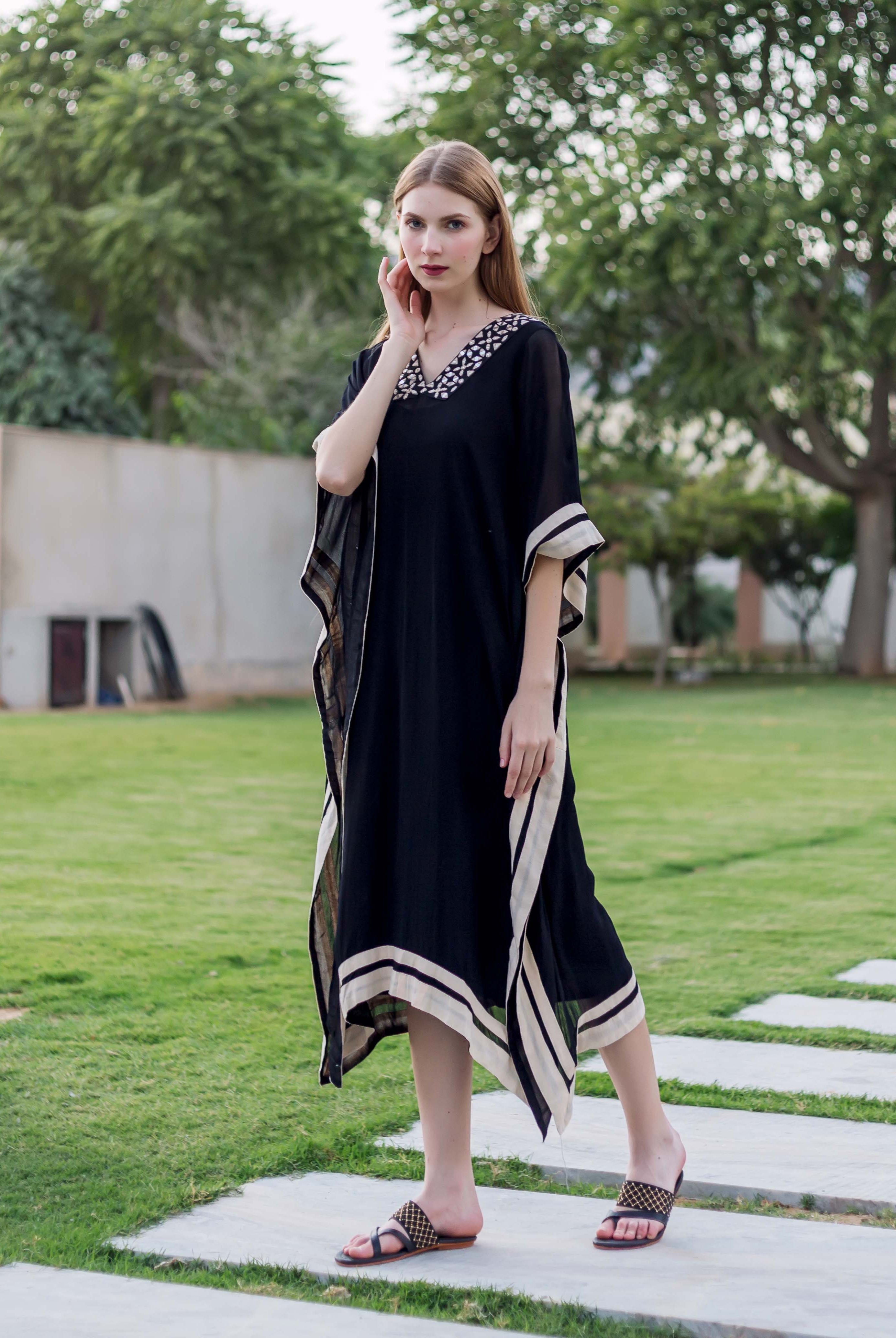 Front view model wearing black kaftan with white embroidered V-neck and striped trim.