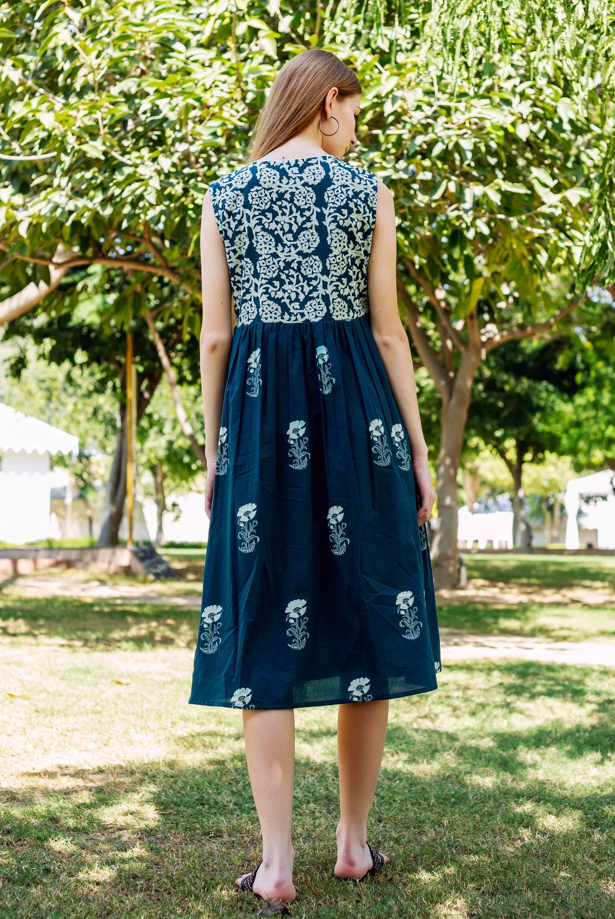 Rear view of model wearing a teal green hand-block-printed ethnic floral sleeveless midi dress.