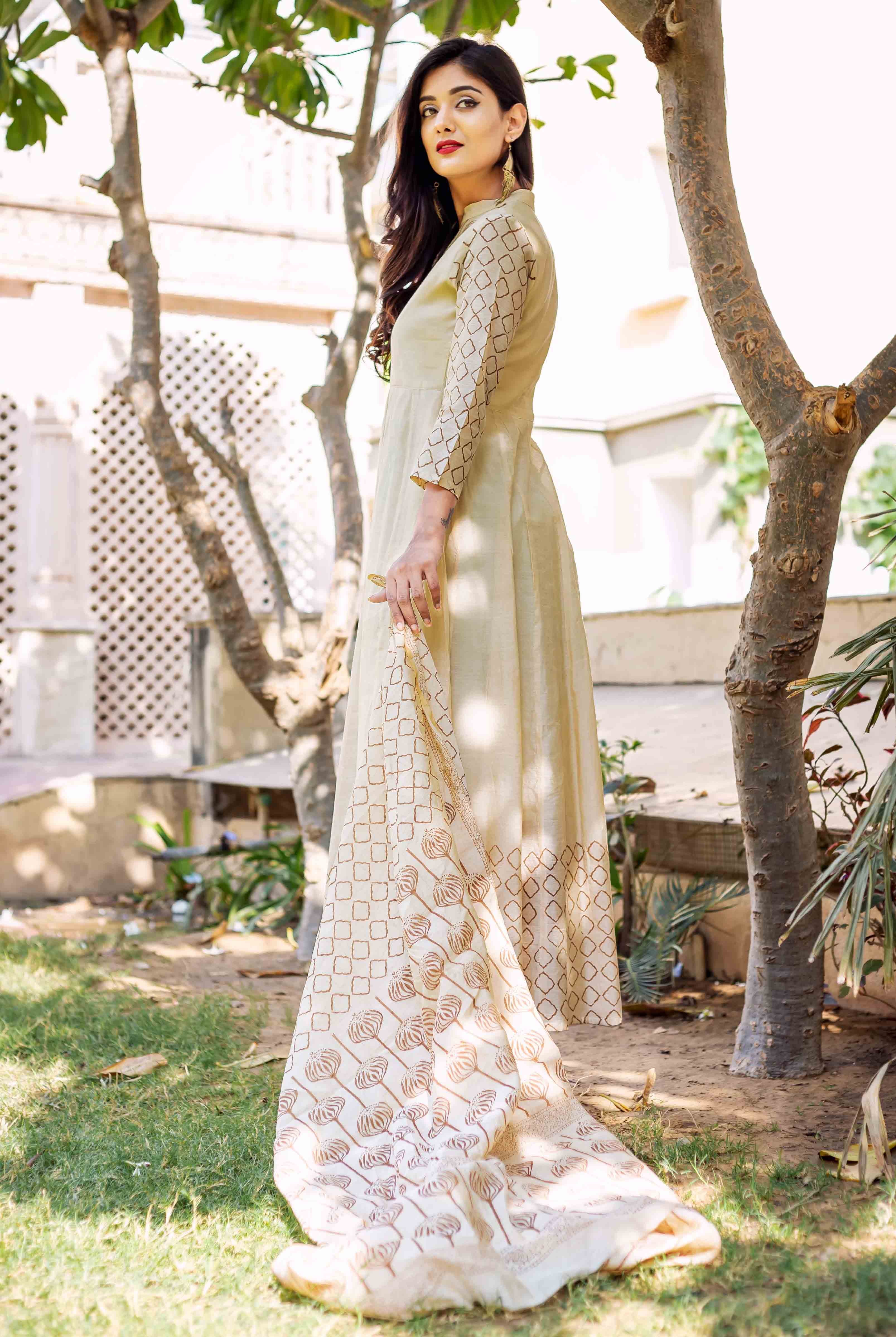 A model wearing a beige and brown printed dress, standing outdoors.