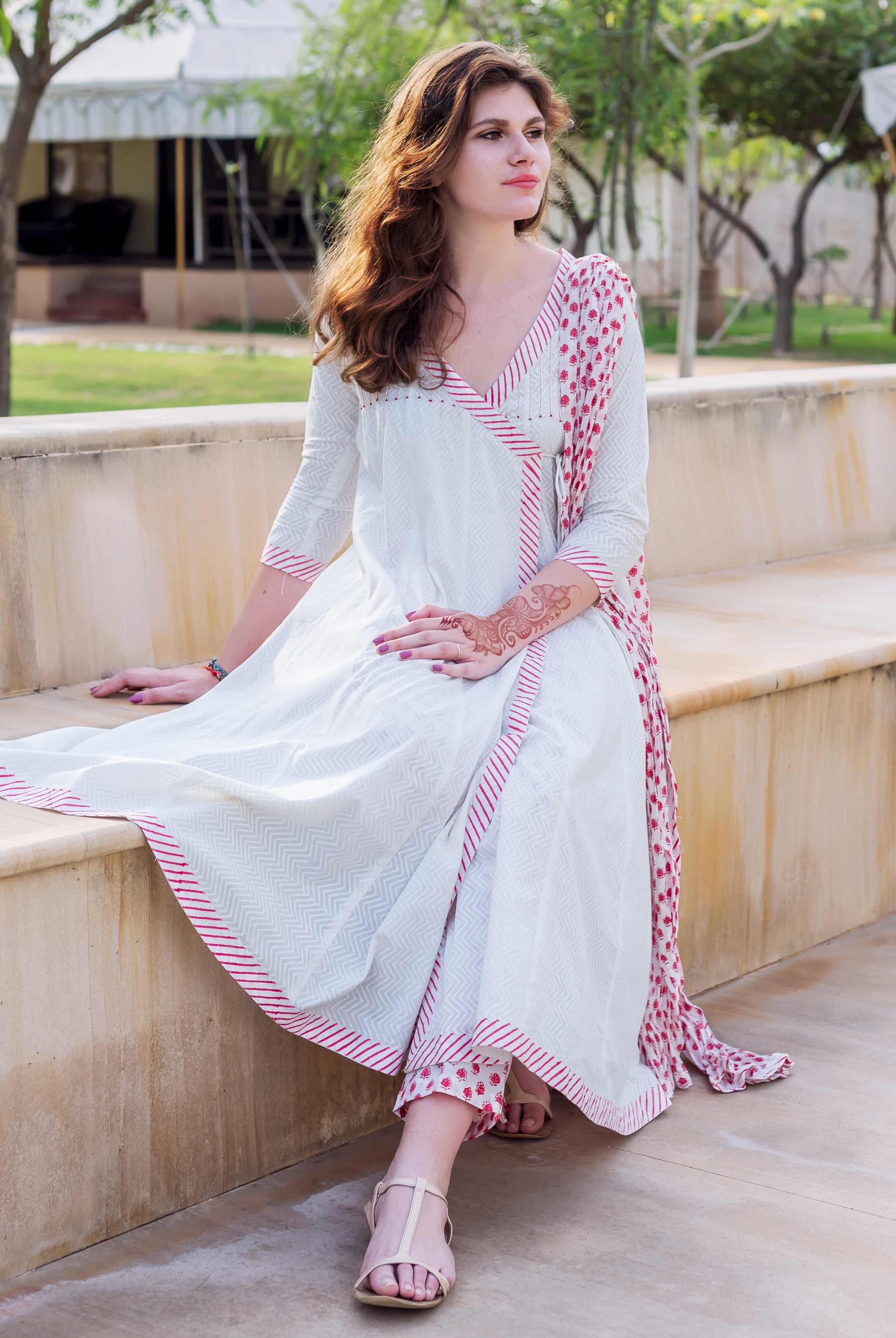 White and red Angrakha dress with hand-block printed patterns, worn by a sitting woman.