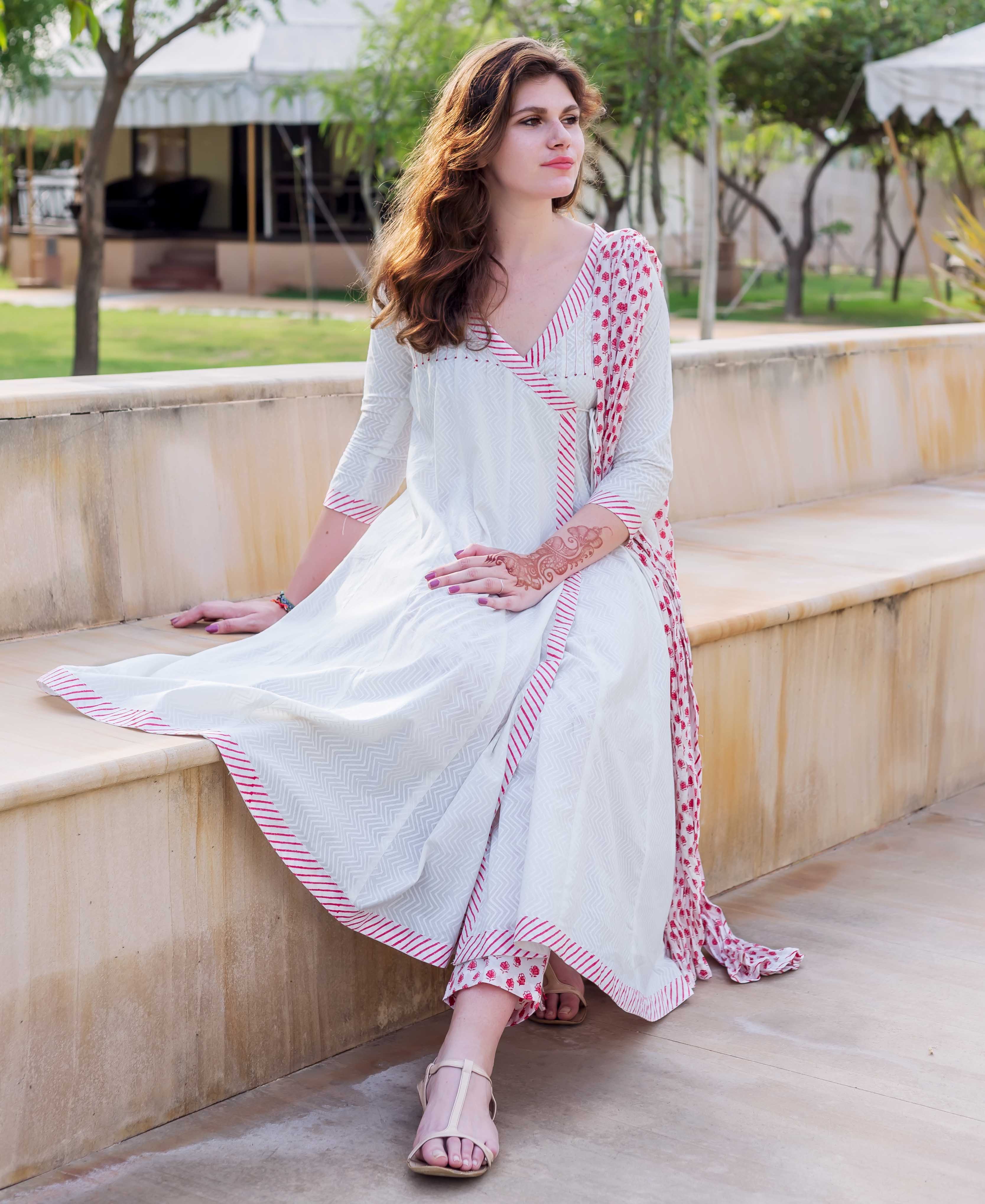 White and red Angrakha dress with hand-block printed patterns, worn by a sitting woman.