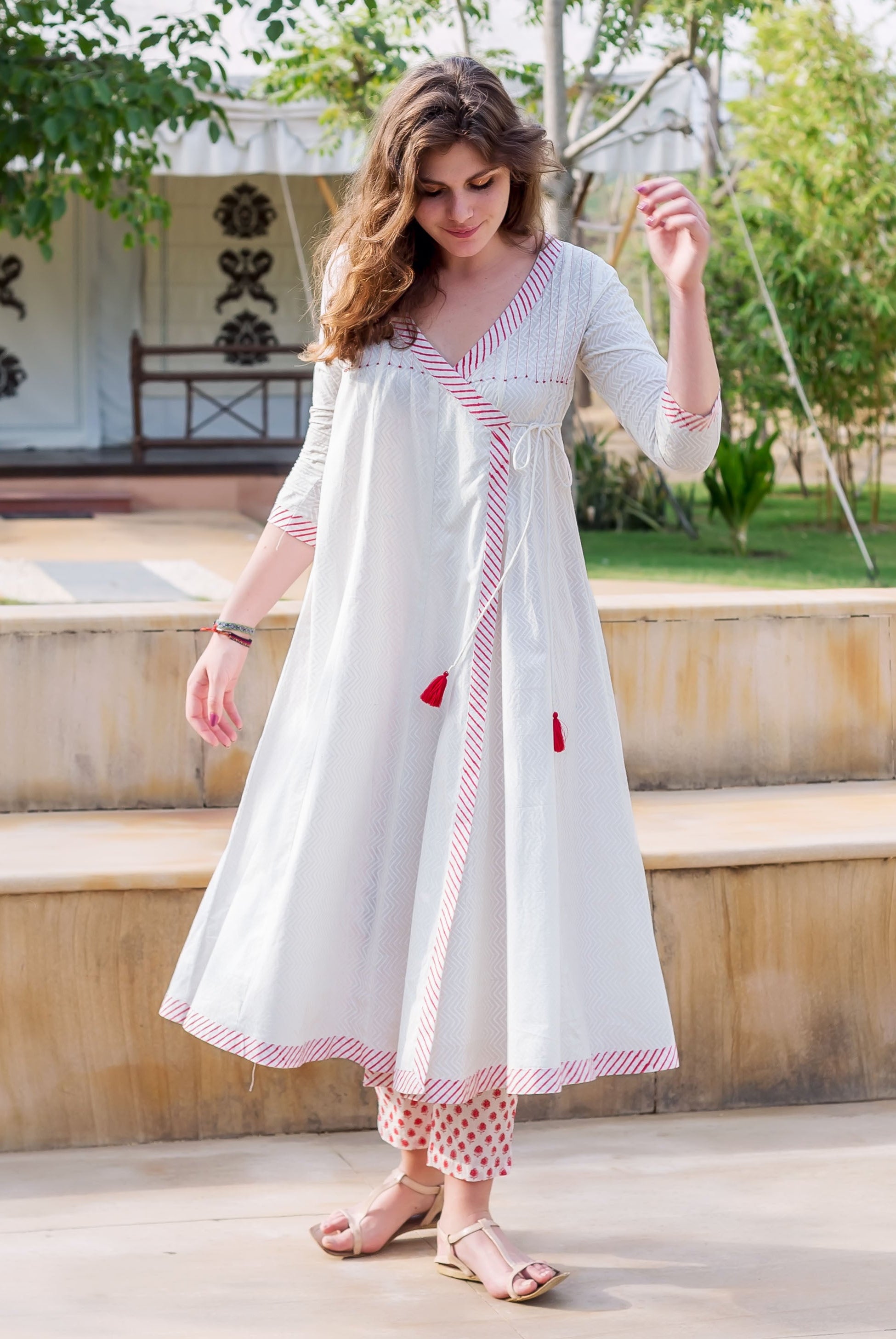 Standing model in white and red Angrakha dress with chevron print, matching polka dot pants.