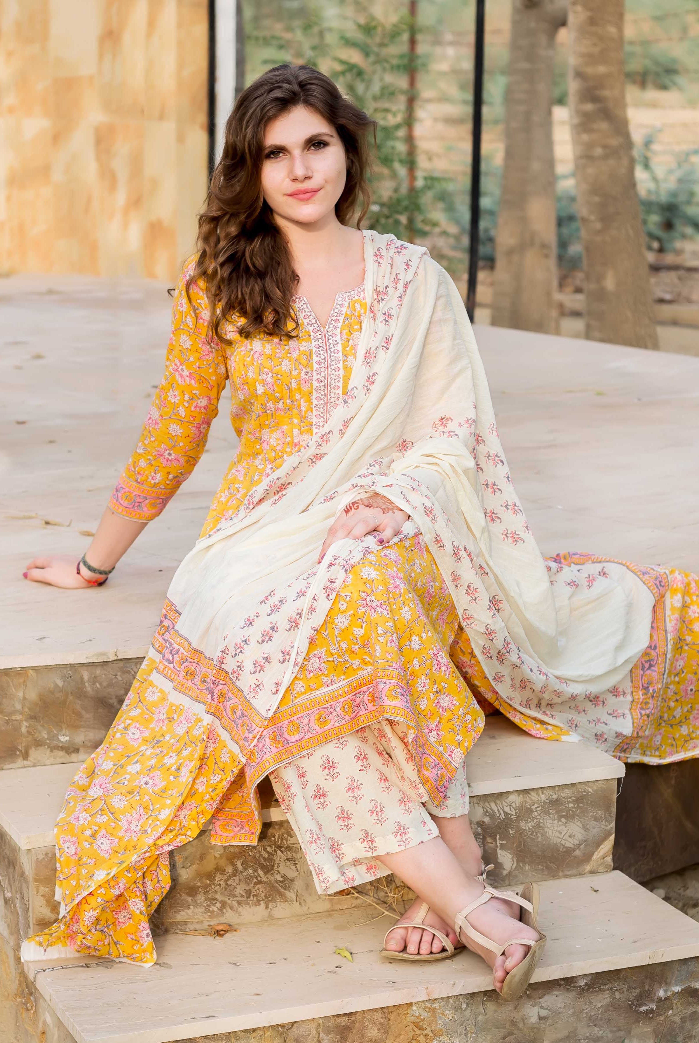 Woman in a yellow Jaal block-printed kurta set with cream dupatta, sitting on steps.