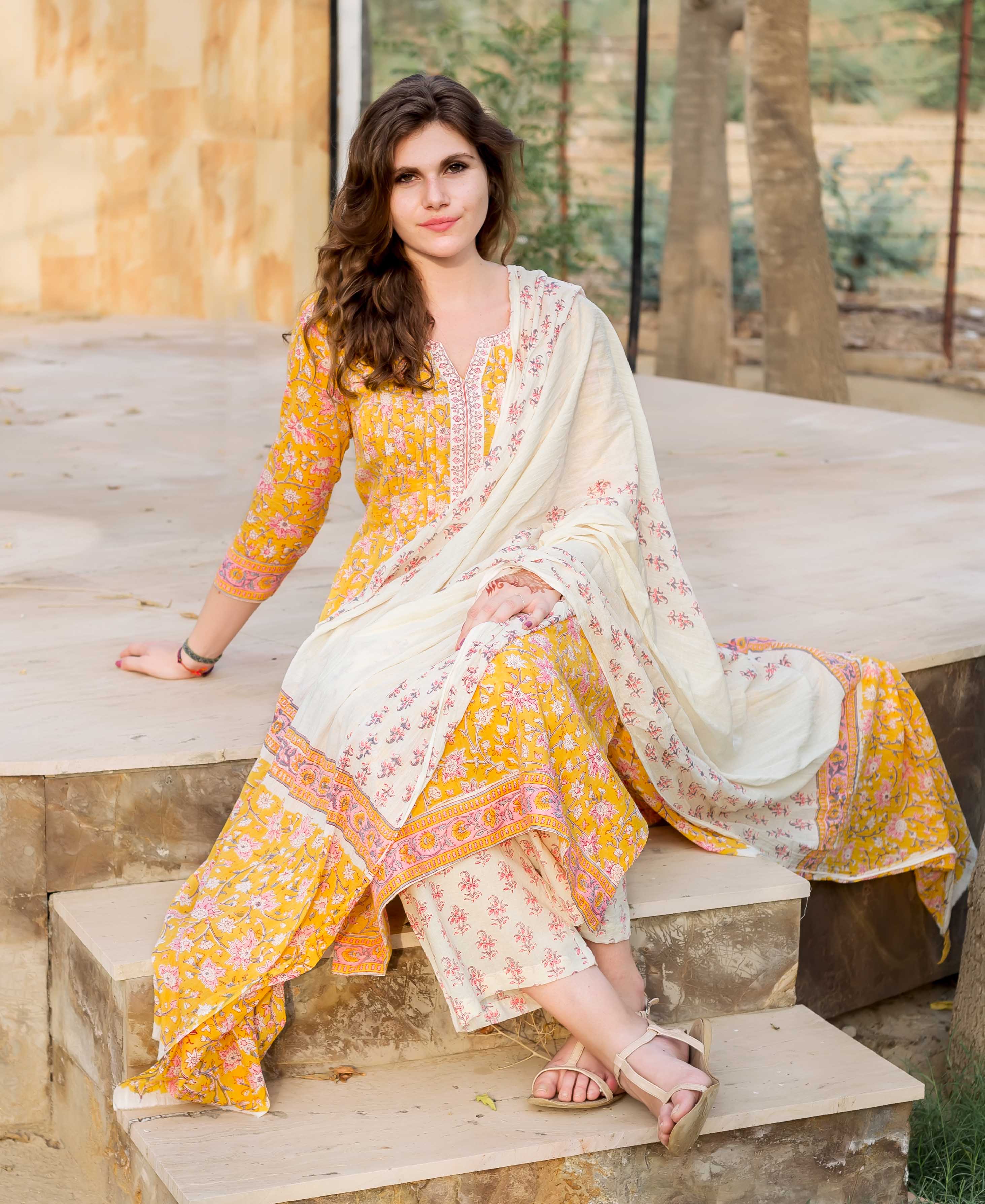 Woman in a yellow Jaal block-printed kurta set with cream dupatta, sitting on steps.
