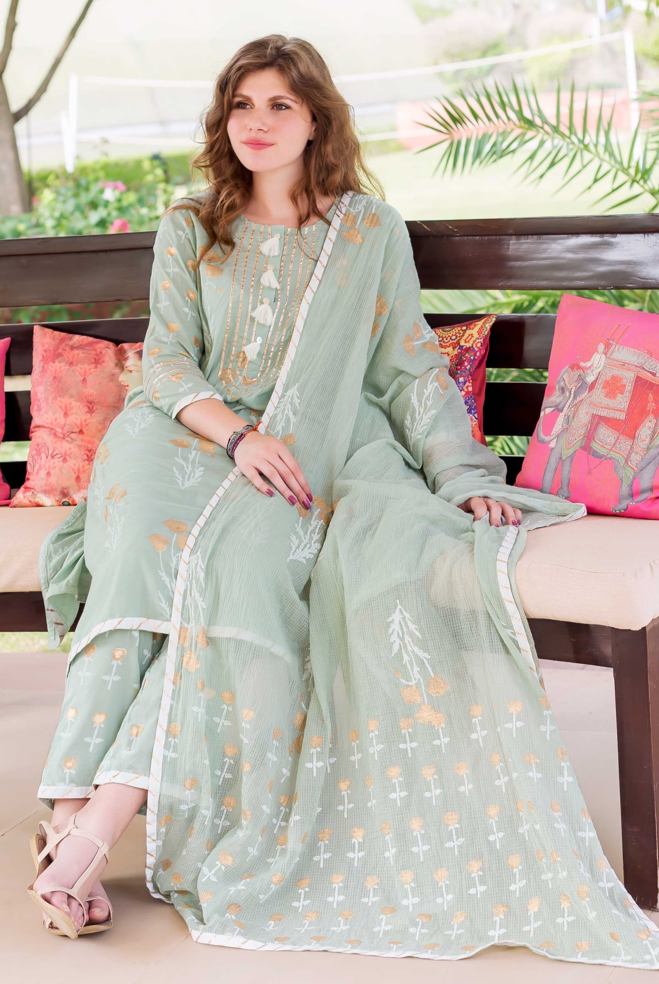 Model seated, wearing mint green cotton hand-block printed ethnic kurta set with golden patterns.