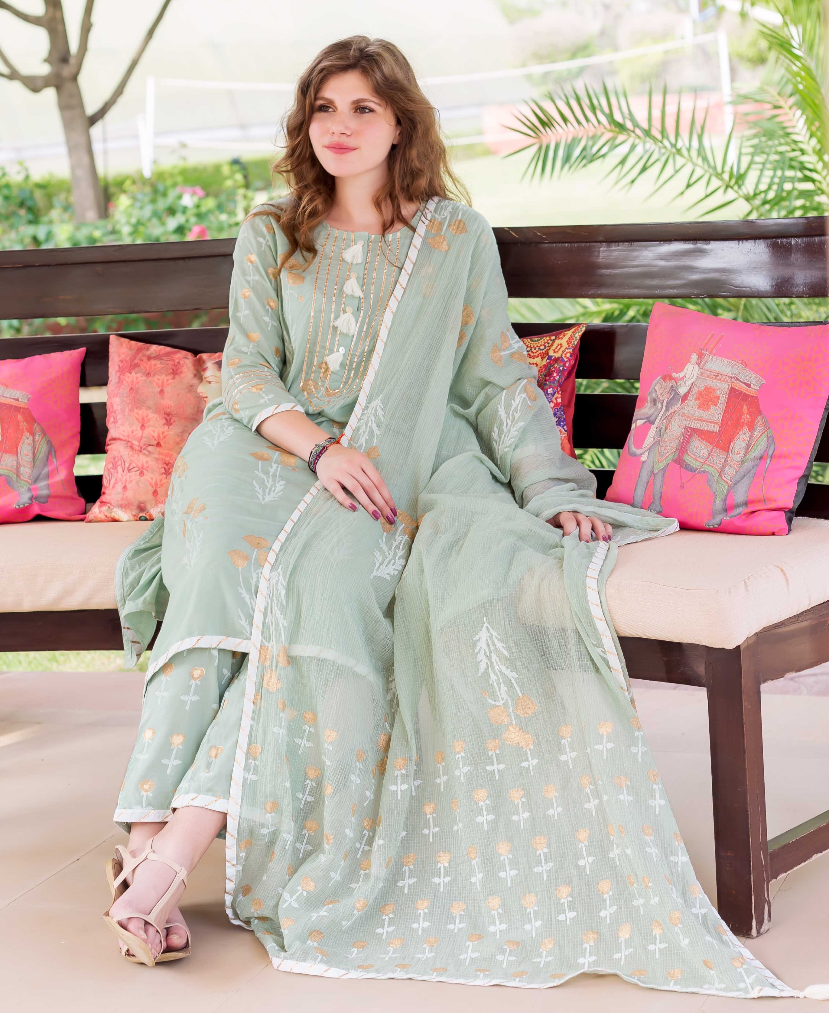 Model seated, wearing mint green cotton hand-block printed ethnic kurta set with golden patterns.