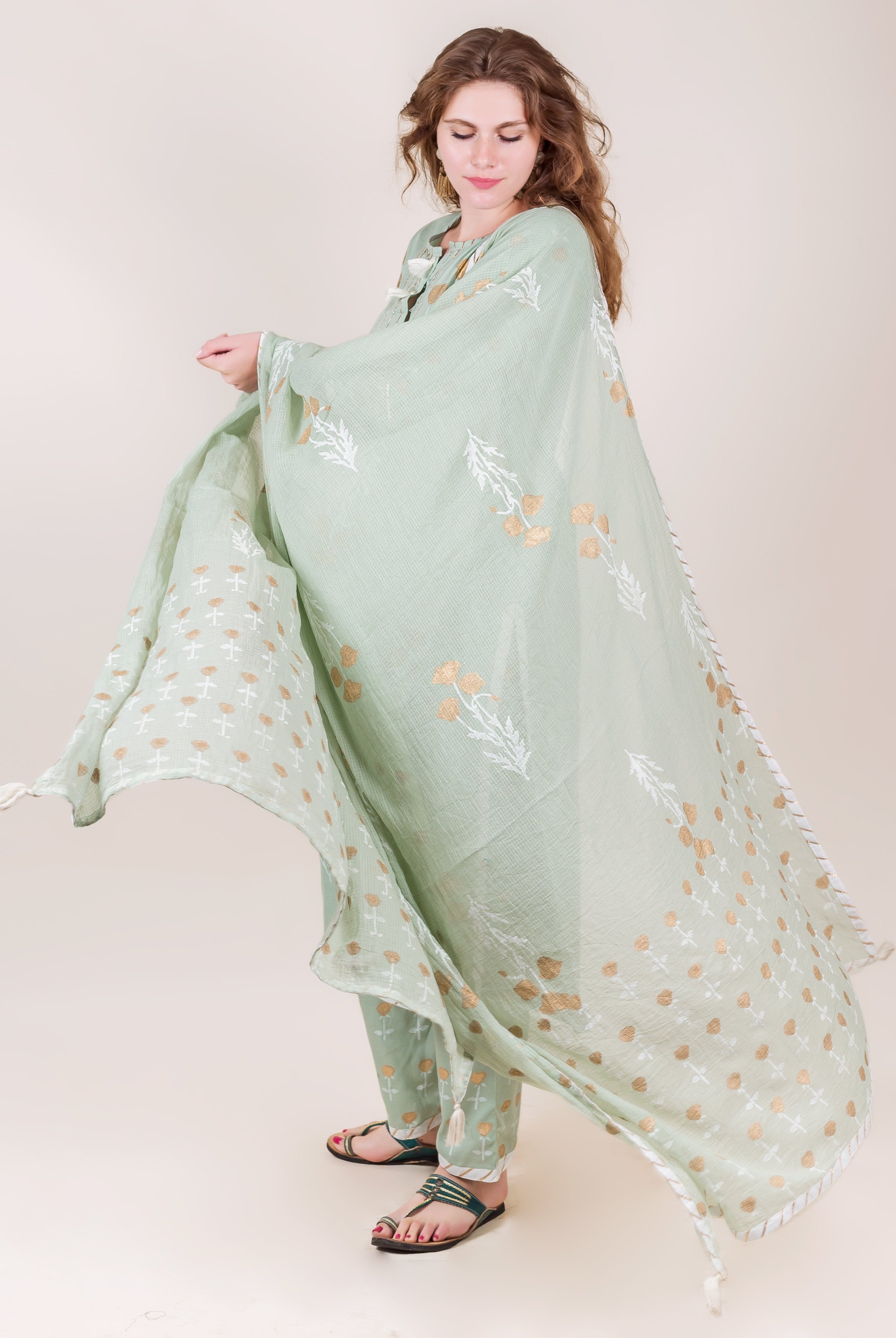 Model wearing flowing mint green cotton kurta set with gold hand-block floral prints.