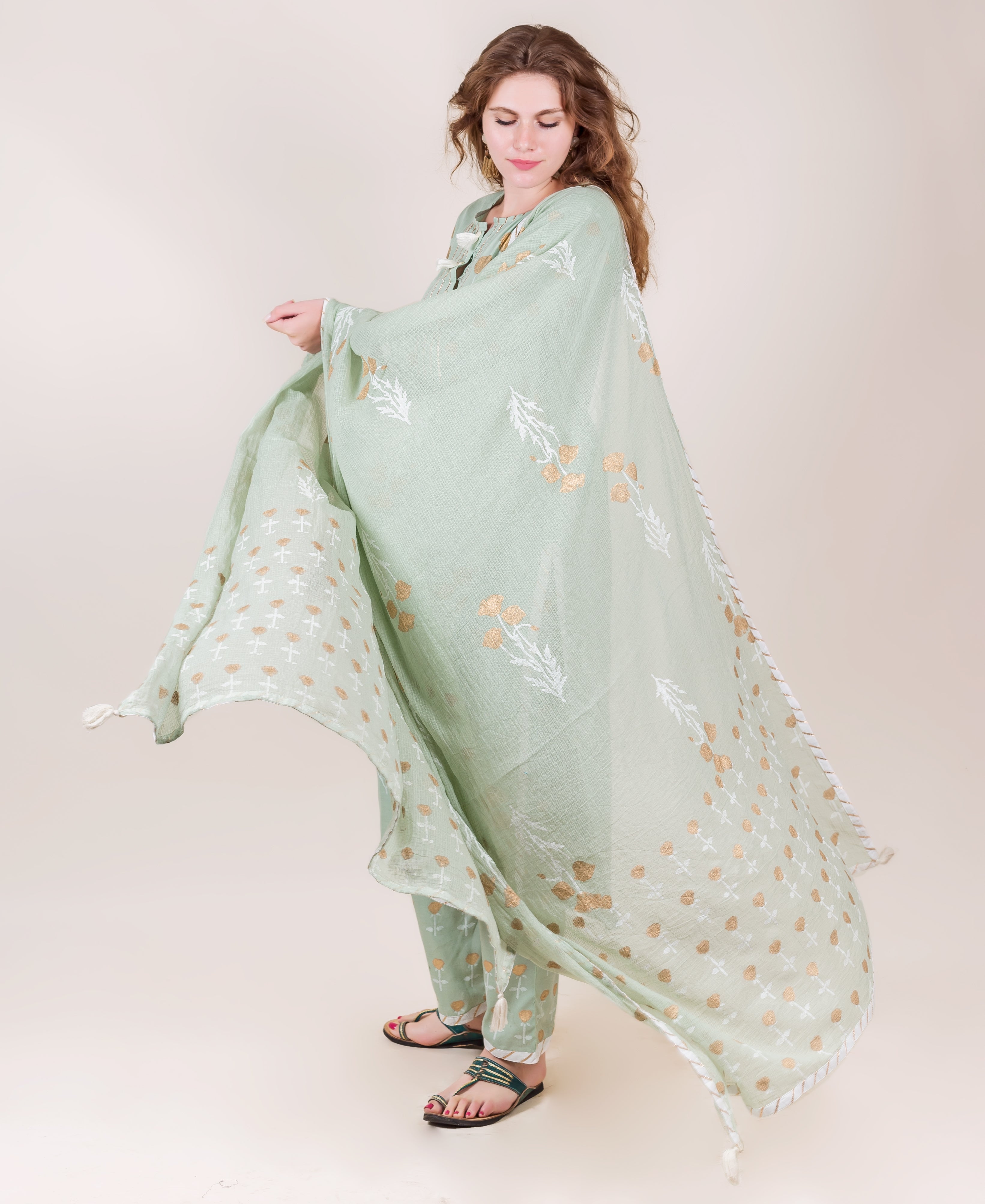 Model wearing flowing mint green cotton kurta set with gold hand-block floral prints.
