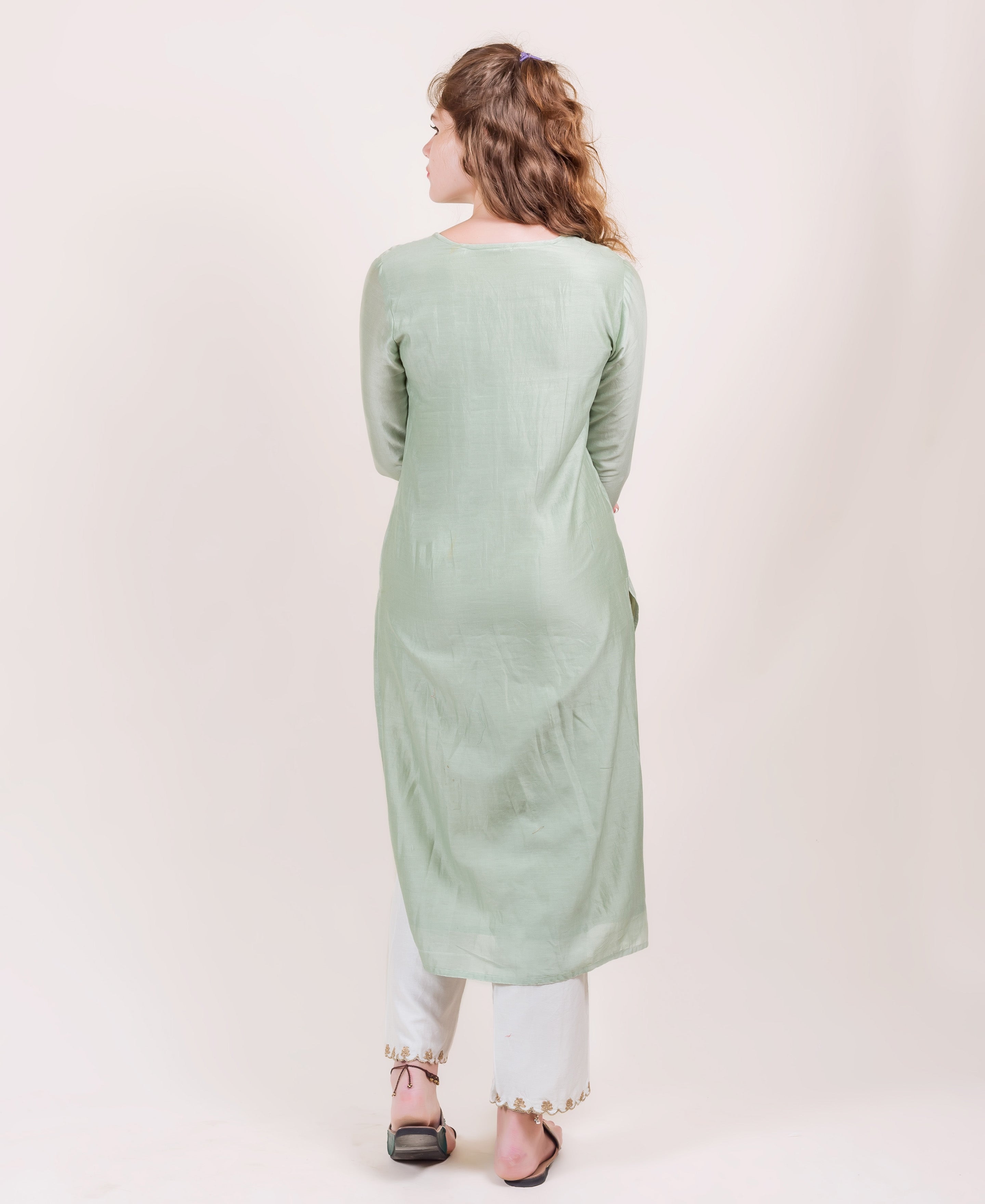 Mint green long tunic on model from behind, with white pants and brown sandals.