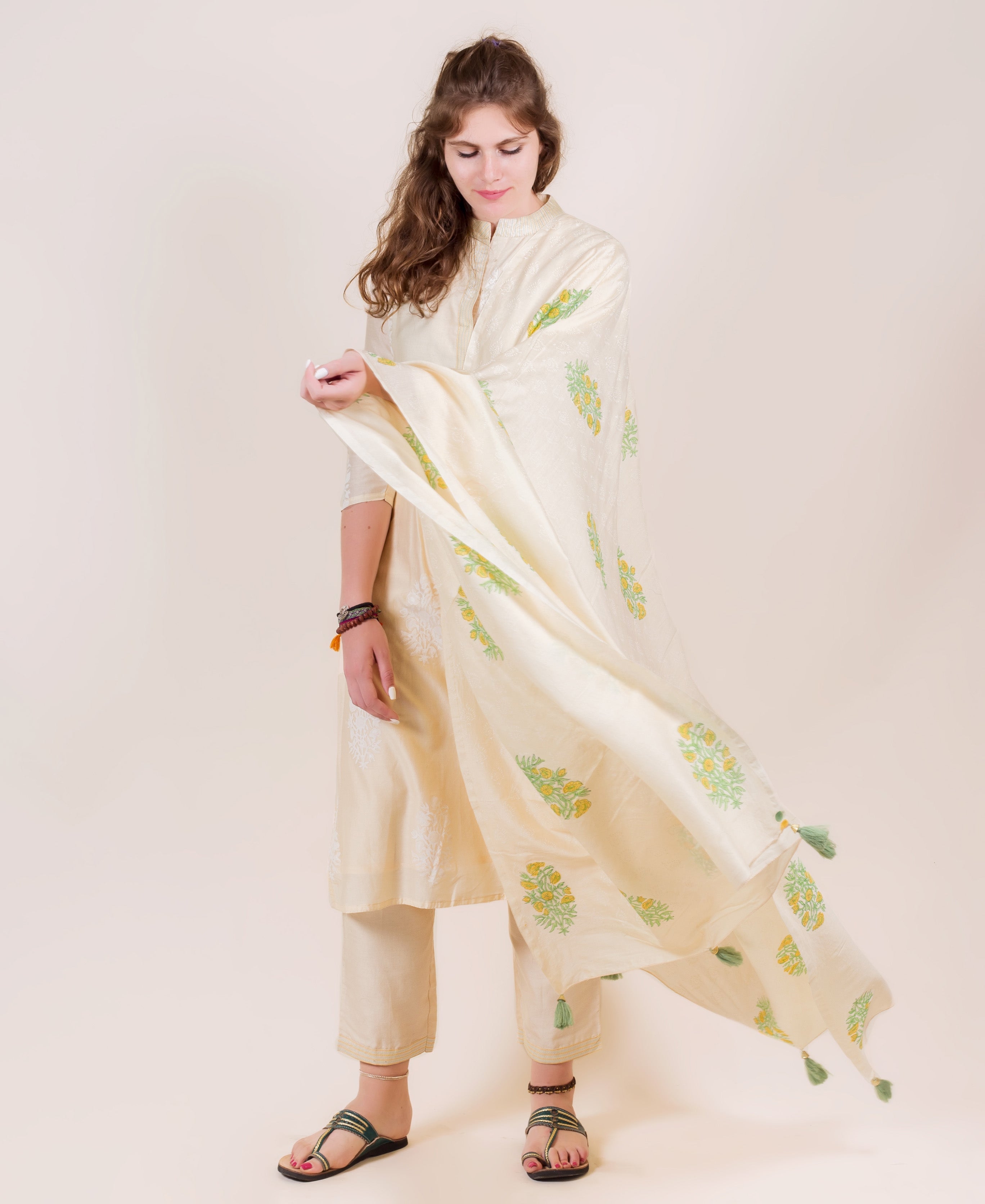 Cream kurta and pants with green and yellow floral dupatta and tassels.