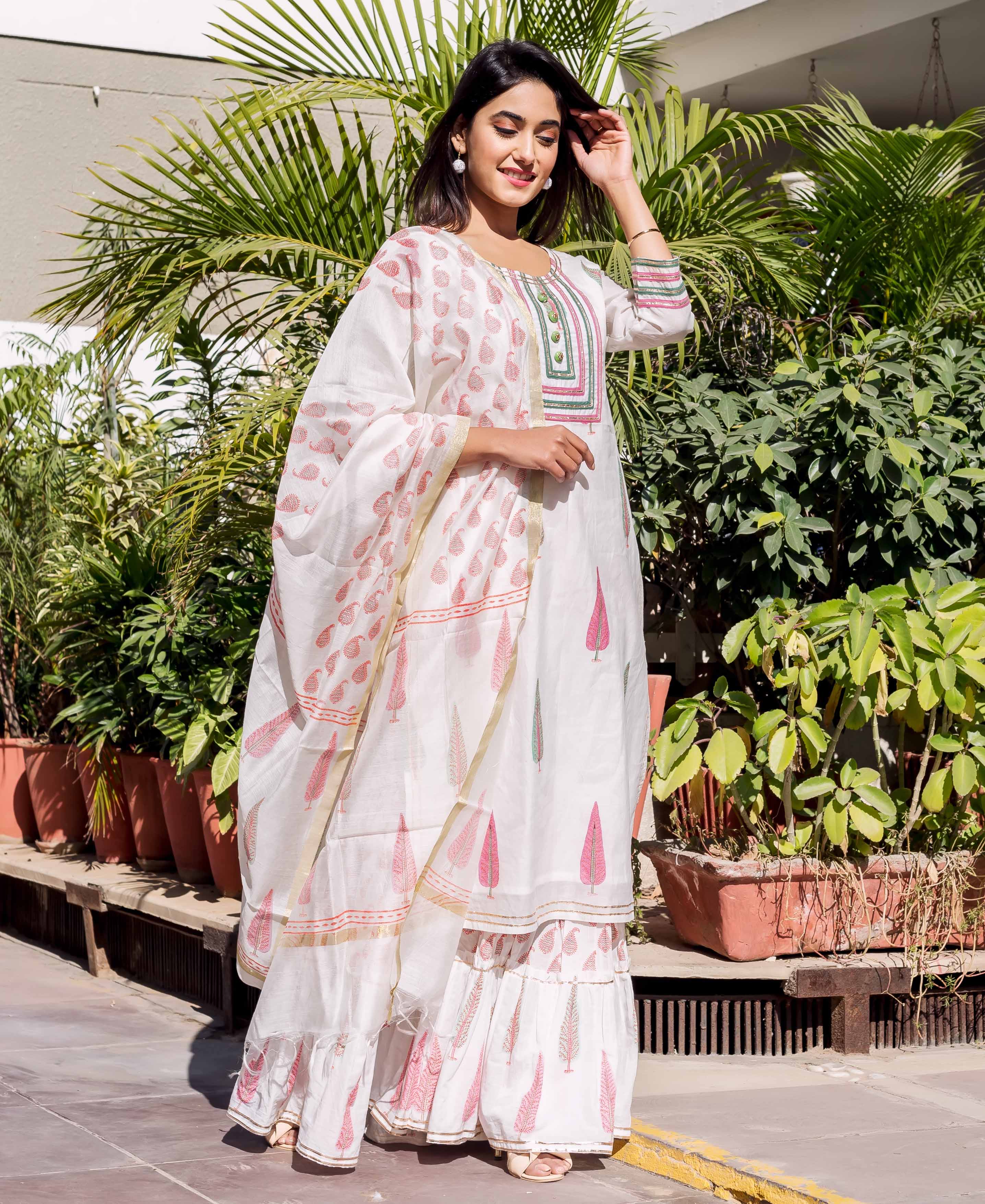 Woman models a white hand-block-printed kurta set with pink paisley dupatta and leaf patterns.