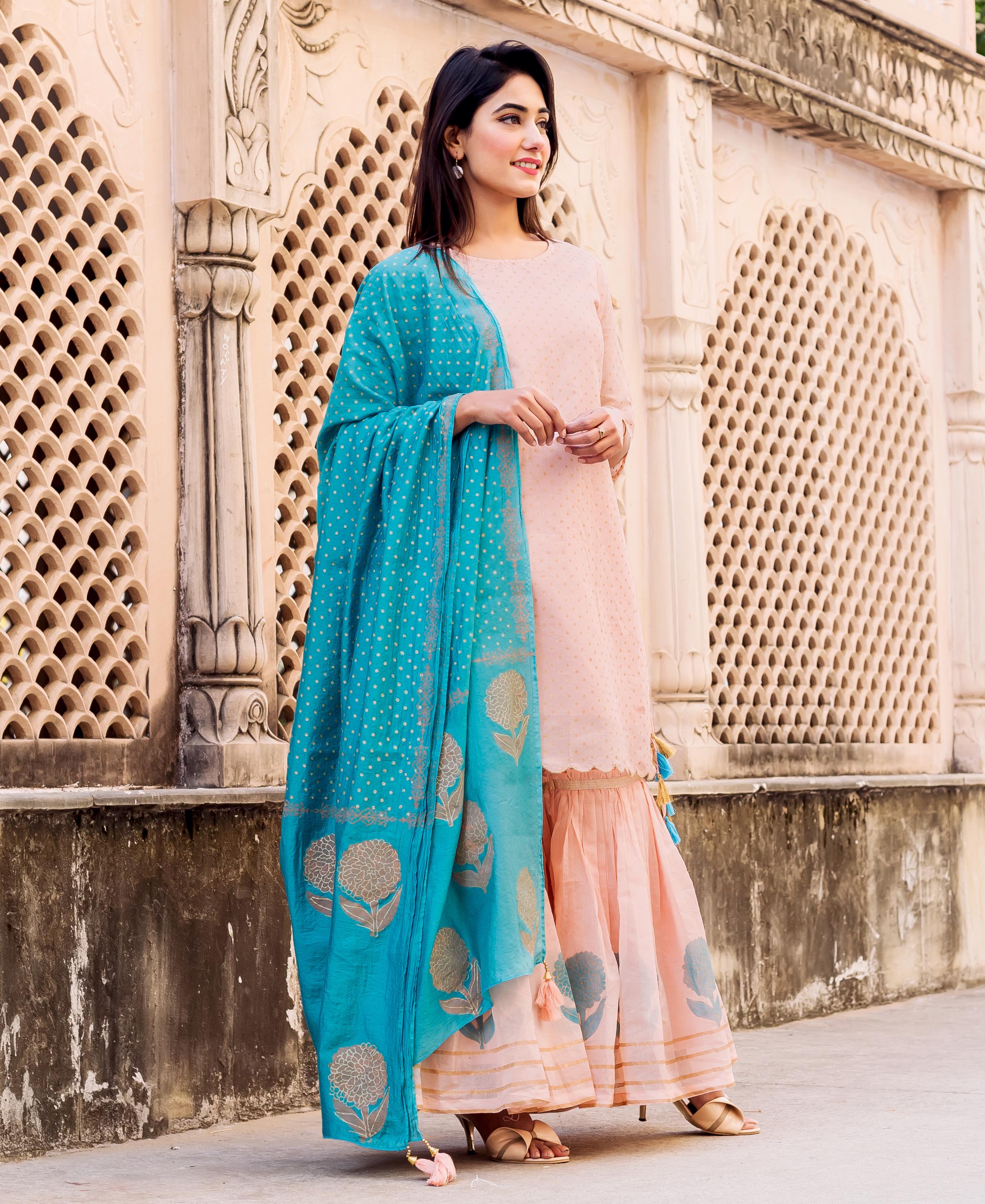 Woman in a peach polka-printed kurta and floral sharara with a blue block-printed dupatta.
