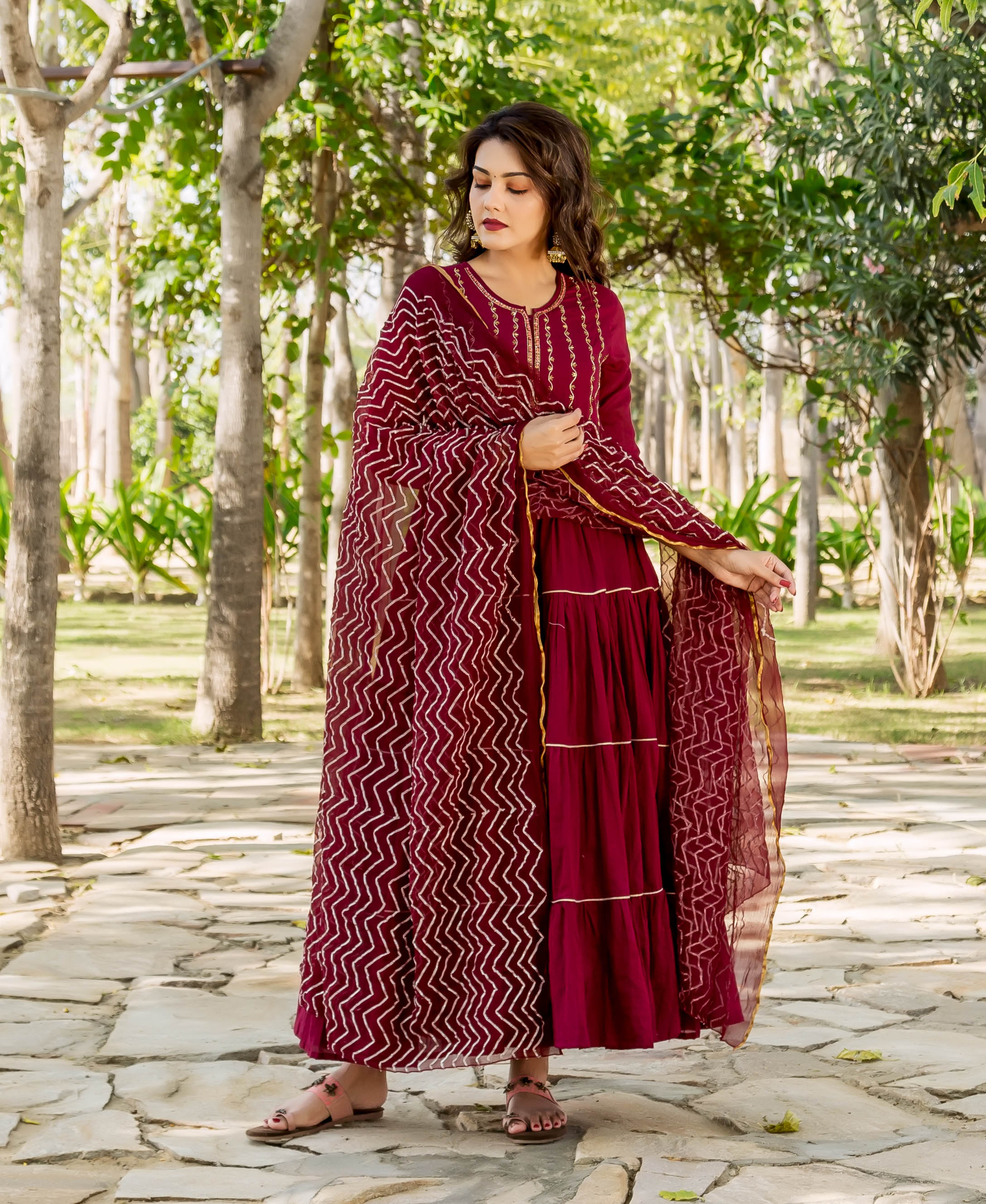 Woman wearing a full-length maroon tiered hand-embroidered dress with a matching zig-zag patterned dupatta.