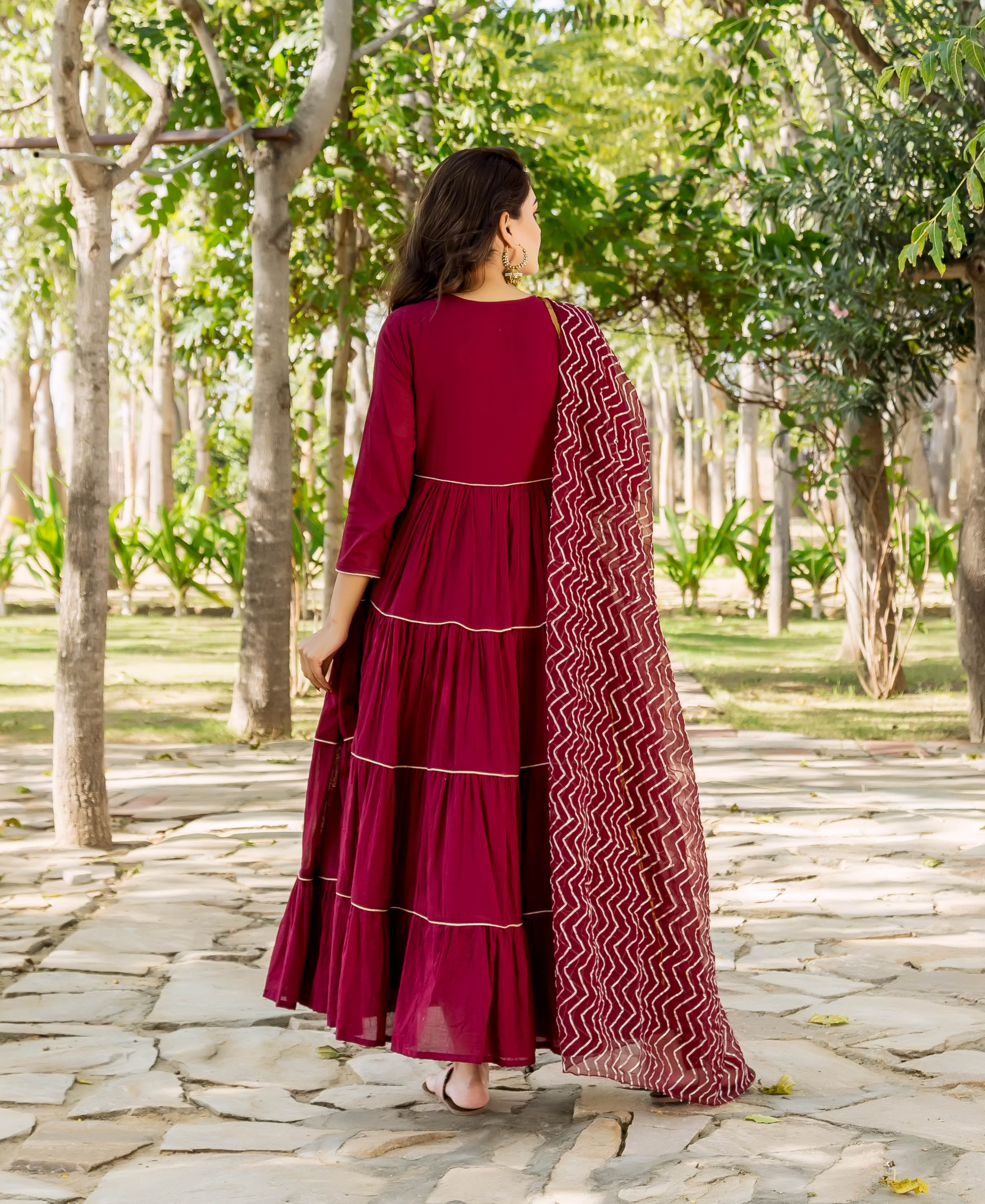 Maroon tiered dress with gold hand embroidery, zig-zag patterned dupatta, worn from behind.