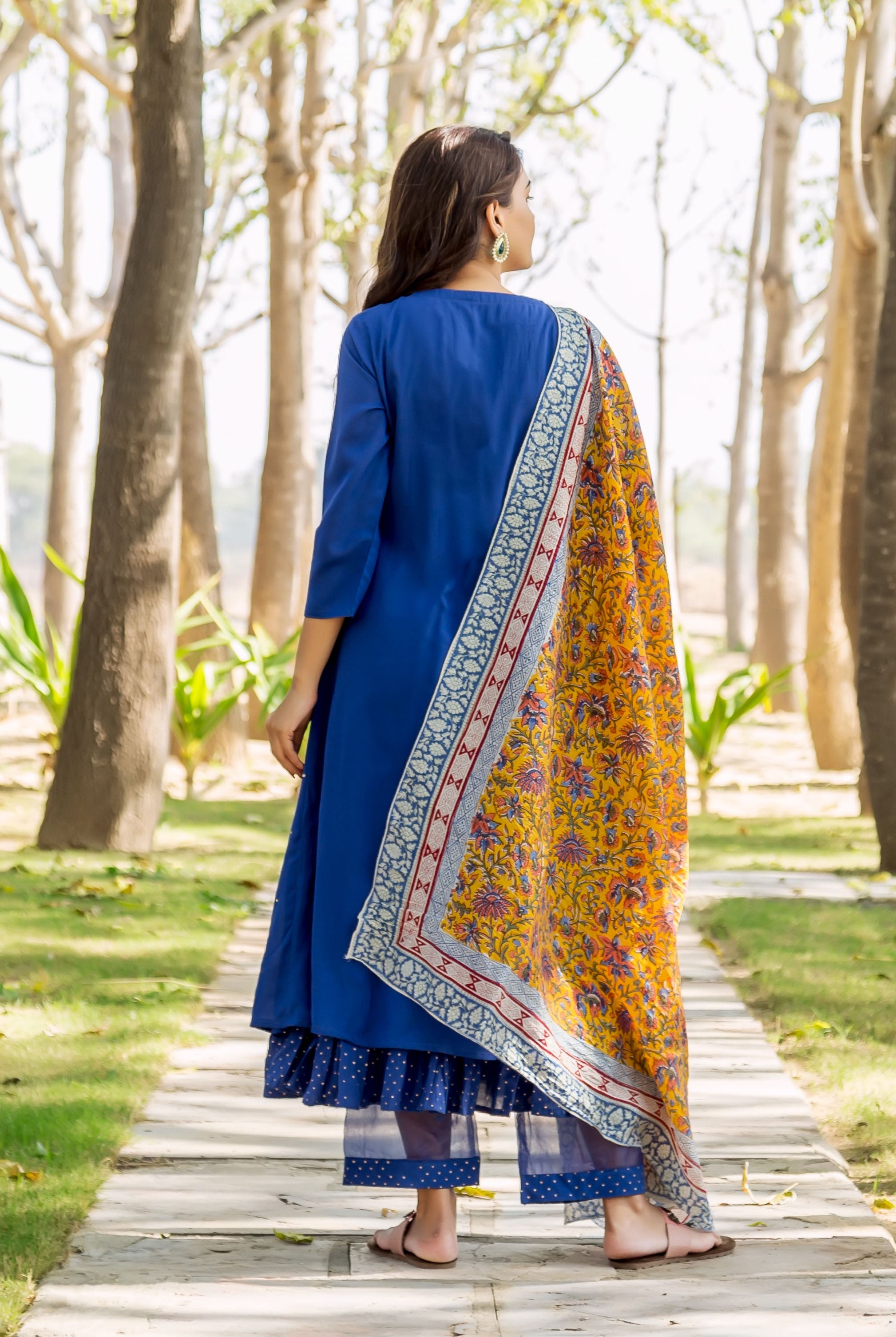 Back view: Model in azure blue layered kurta with yellow floral hand-block-printed dupatta.