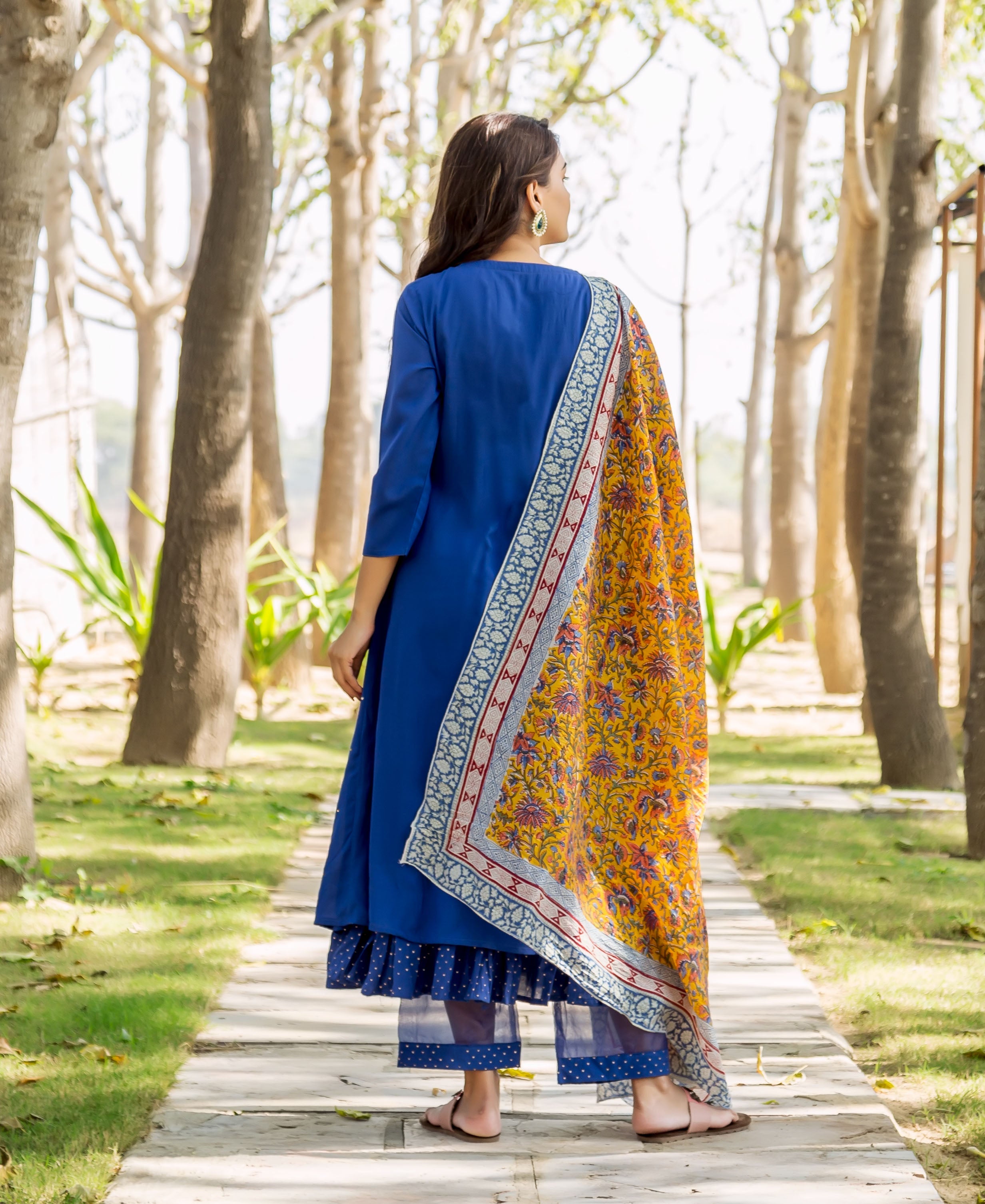 Back view: Model in azure blue layered kurta with yellow floral hand-block-printed dupatta.