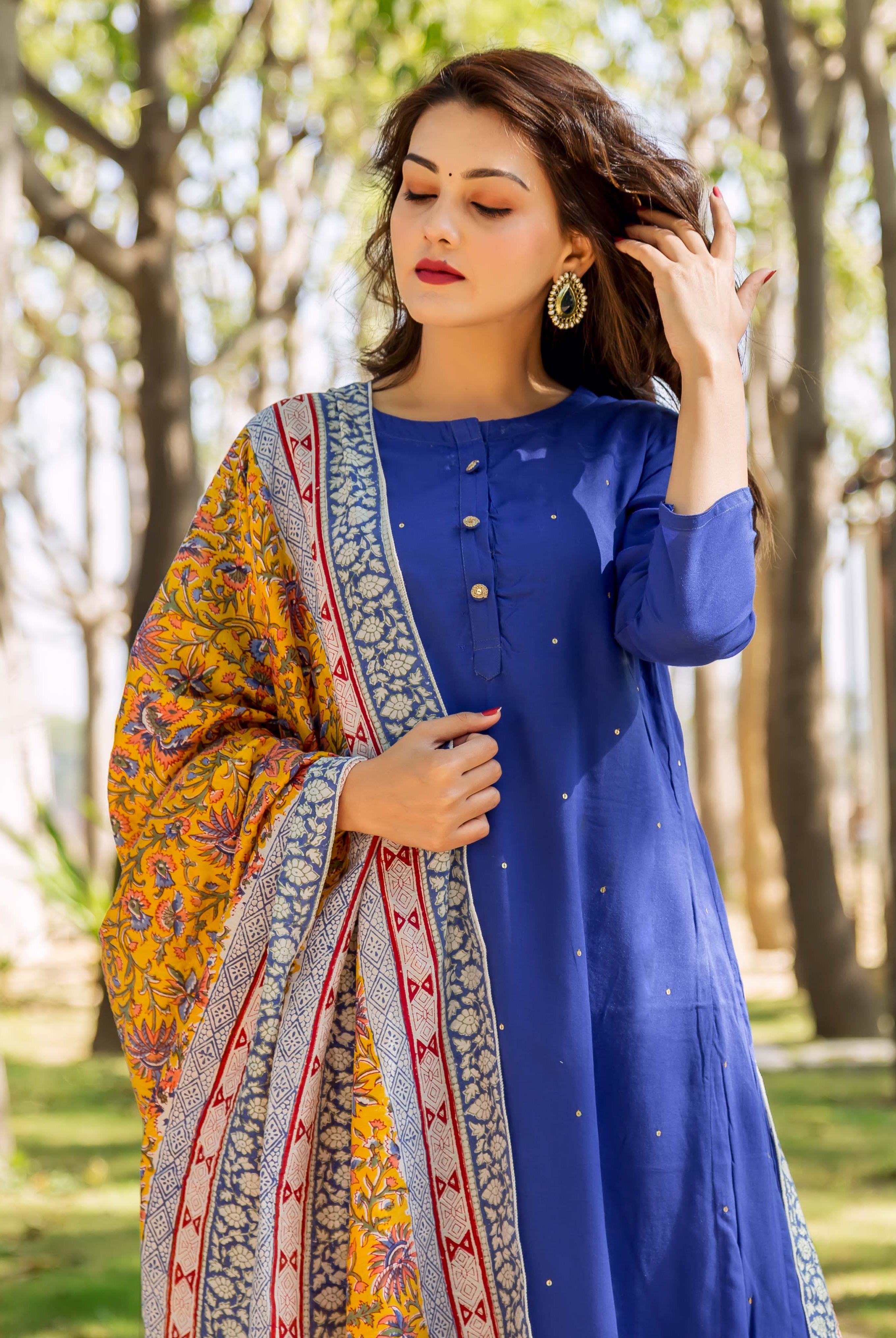 Woman in azure blue embroidered kurta with yellow patterned shawl outdoors.