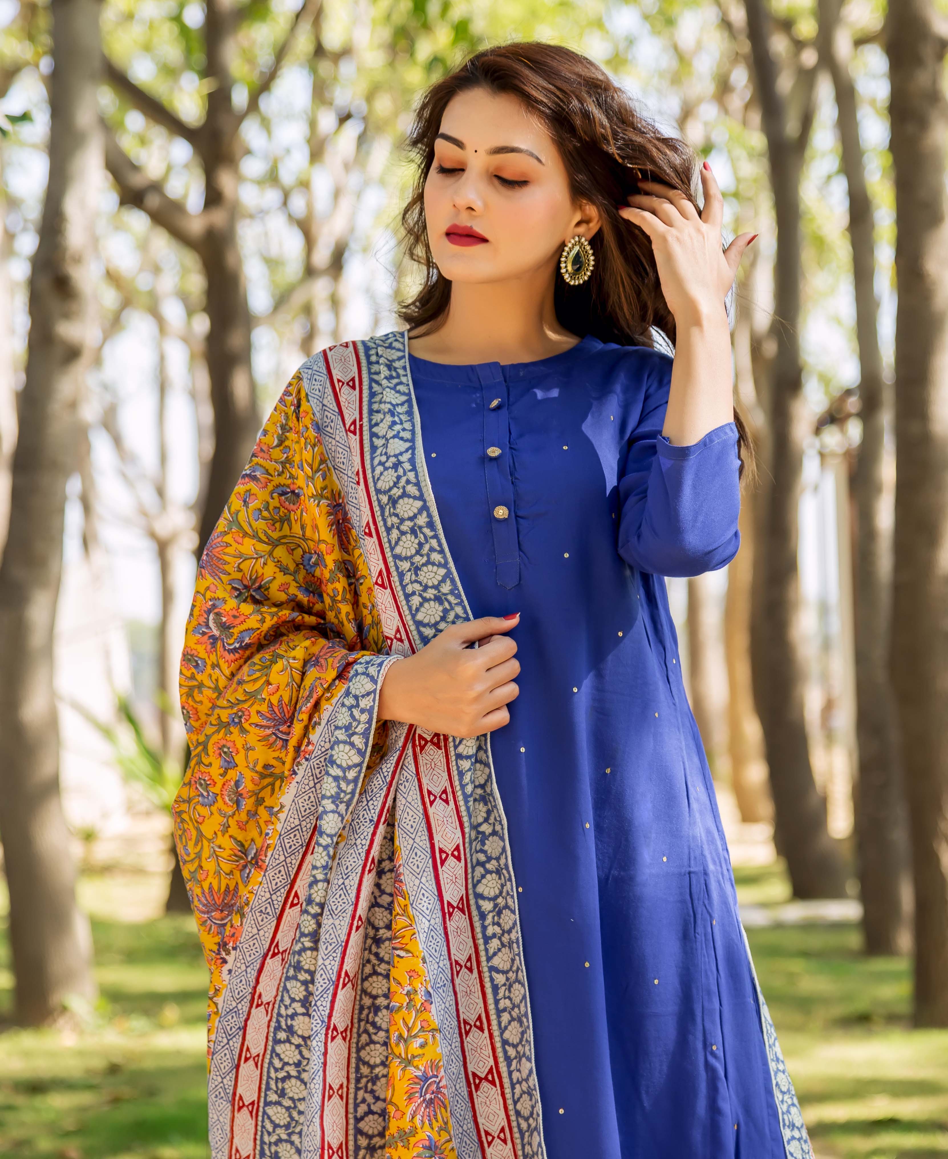Woman in azure blue embroidered kurta with yellow patterned shawl outdoors.