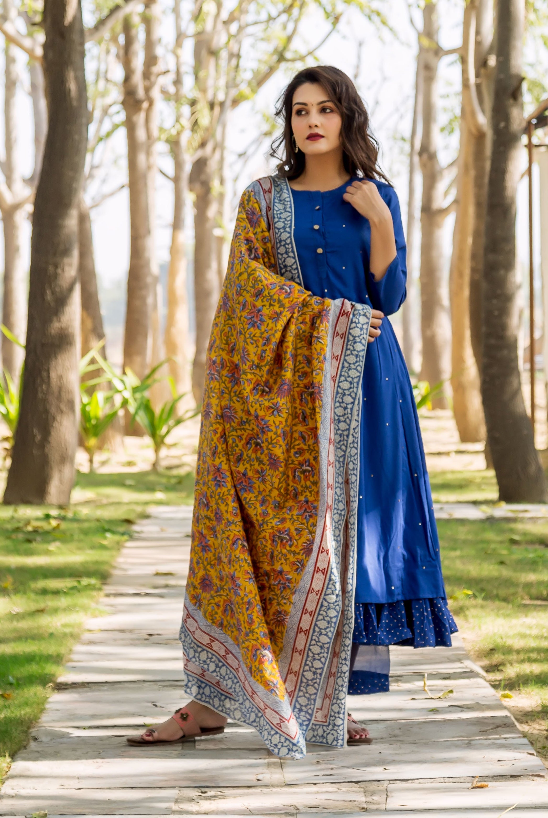 Woman in azure blue embroidered layered kurta with yellow and blue patterned shawl outdoors.