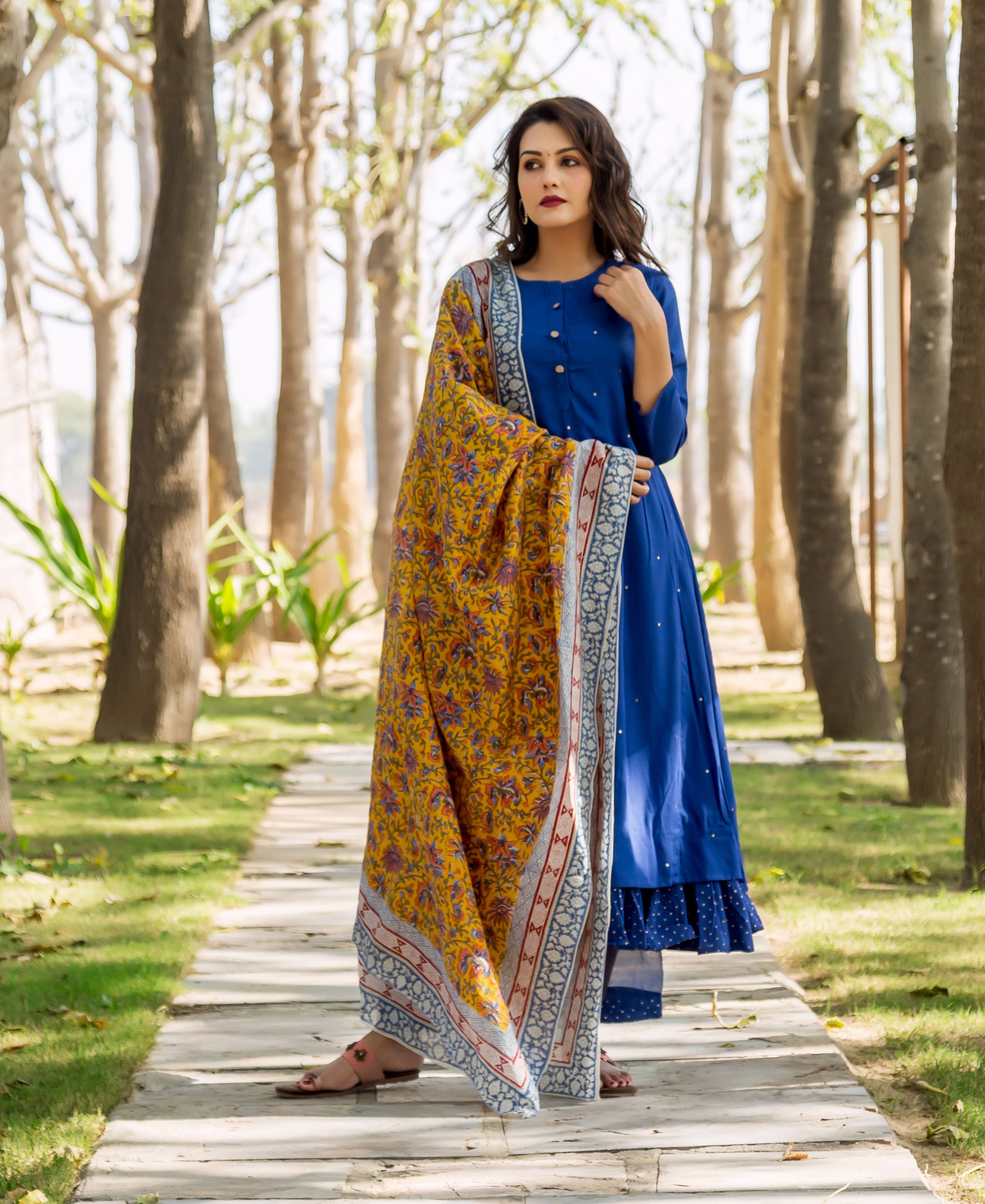 Woman in azure blue embroidered layered kurta with yellow and blue patterned shawl outdoors.