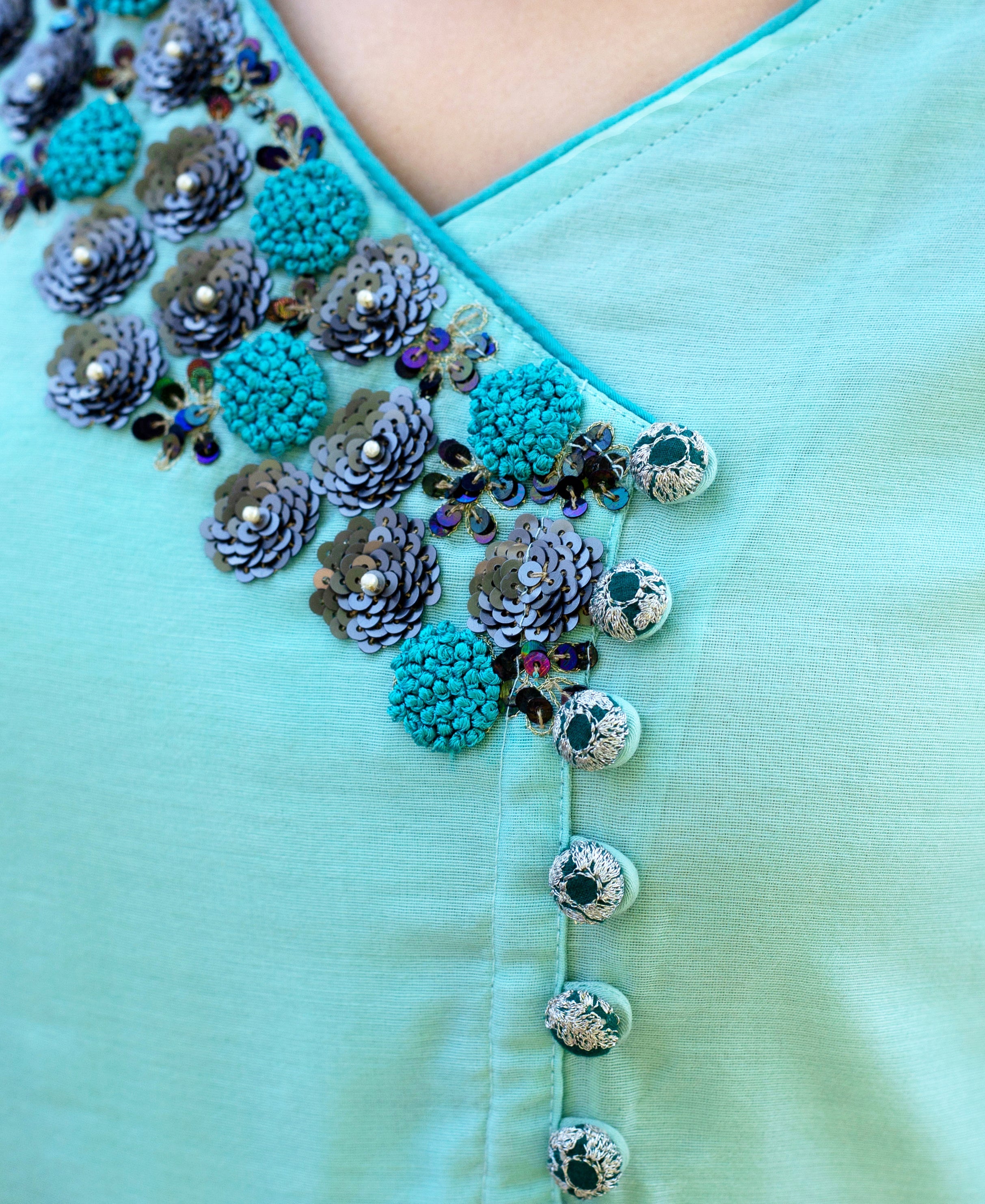 Close-up mint green angrakha dress on model, V-neck with floral sequin embroidery and buttons.