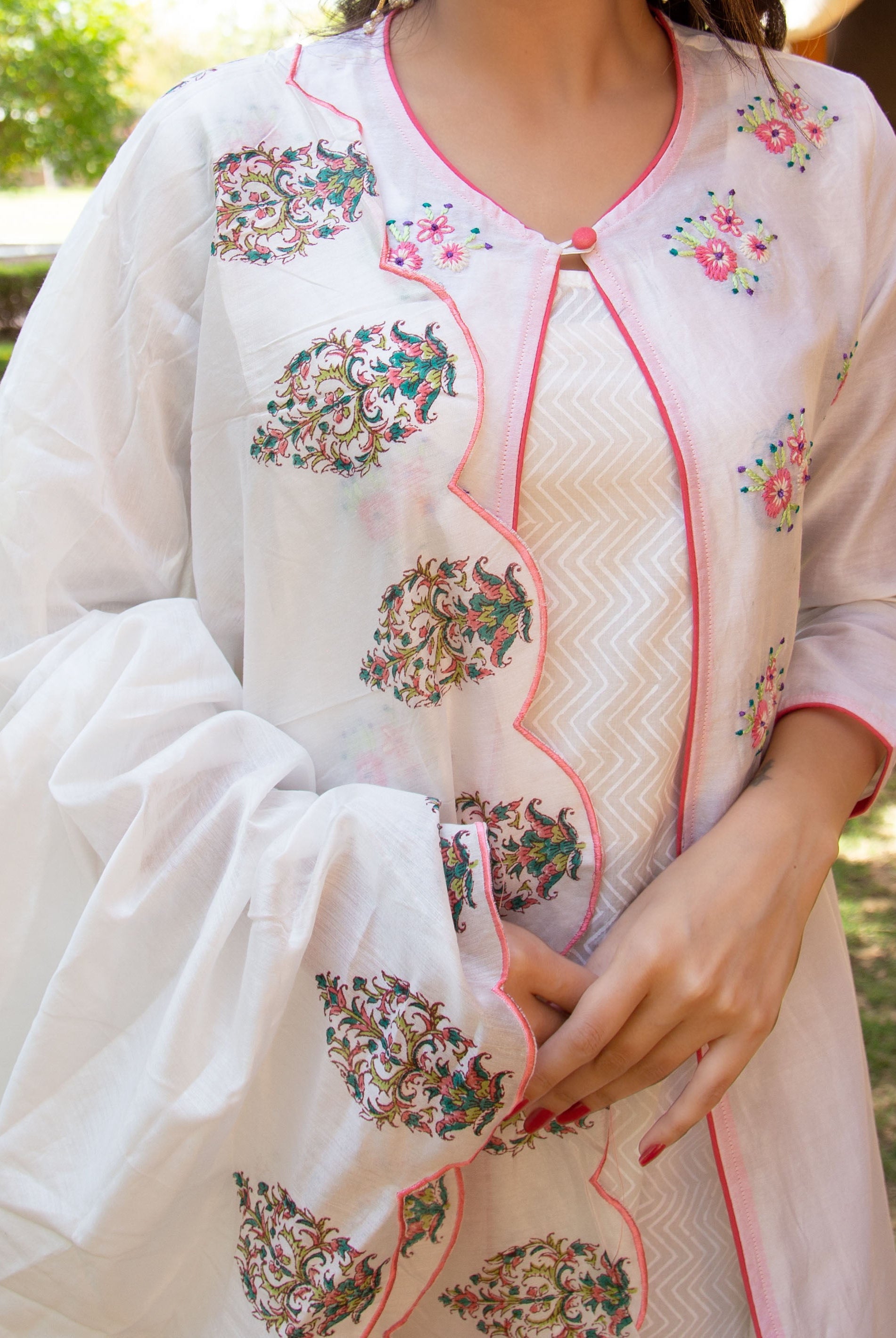 Close-up of model in white layered kurta, pink piping, colourful floral prints, and embroidery.