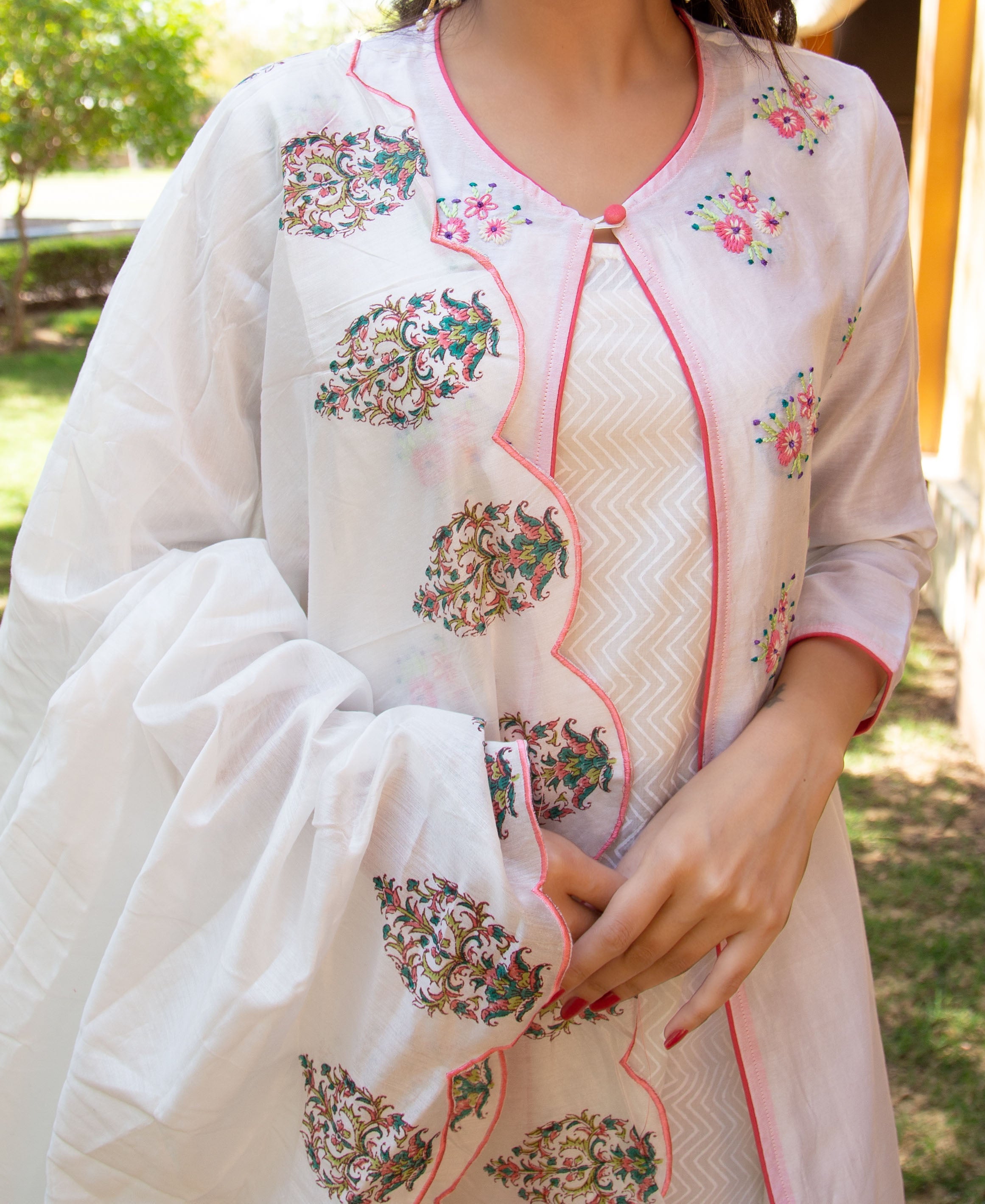 Close-up of model in white layered kurta, pink piping, colourful floral prints, and embroidery.