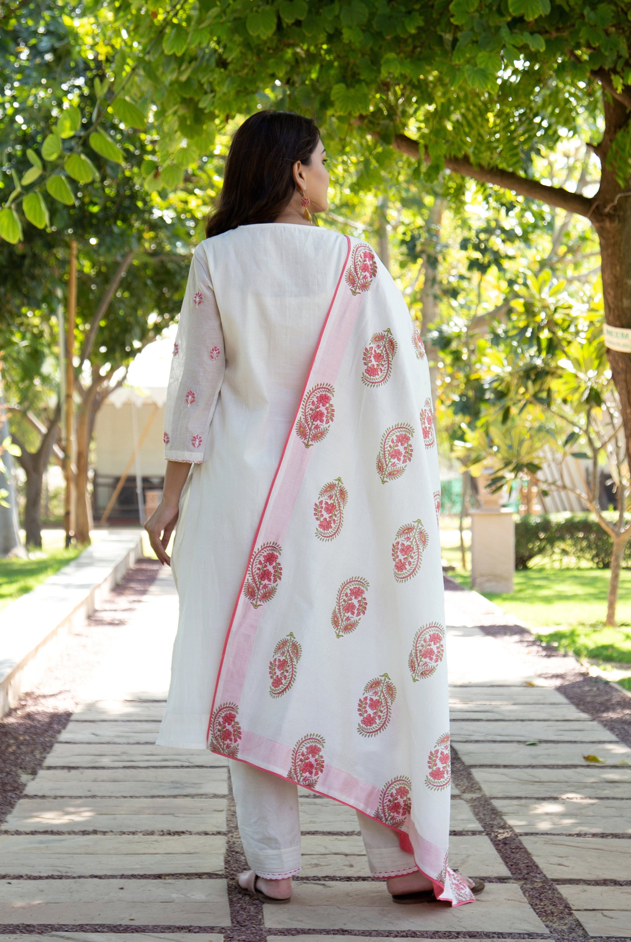 Rear view of model wearing white hand block printed kurta set with pink paisley dupatta.
