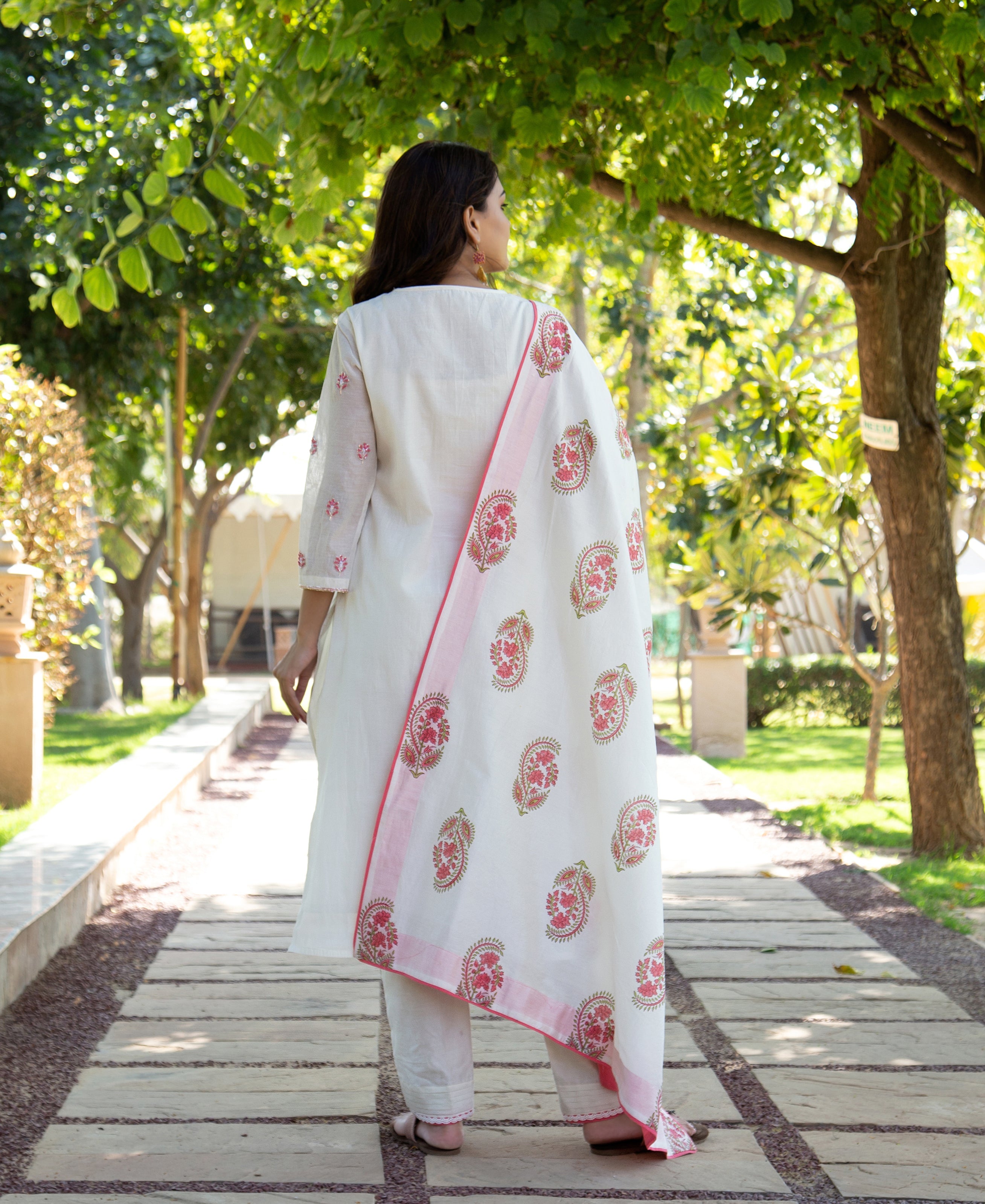 Rear view of model wearing white hand block printed kurta set with pink paisley dupatta.