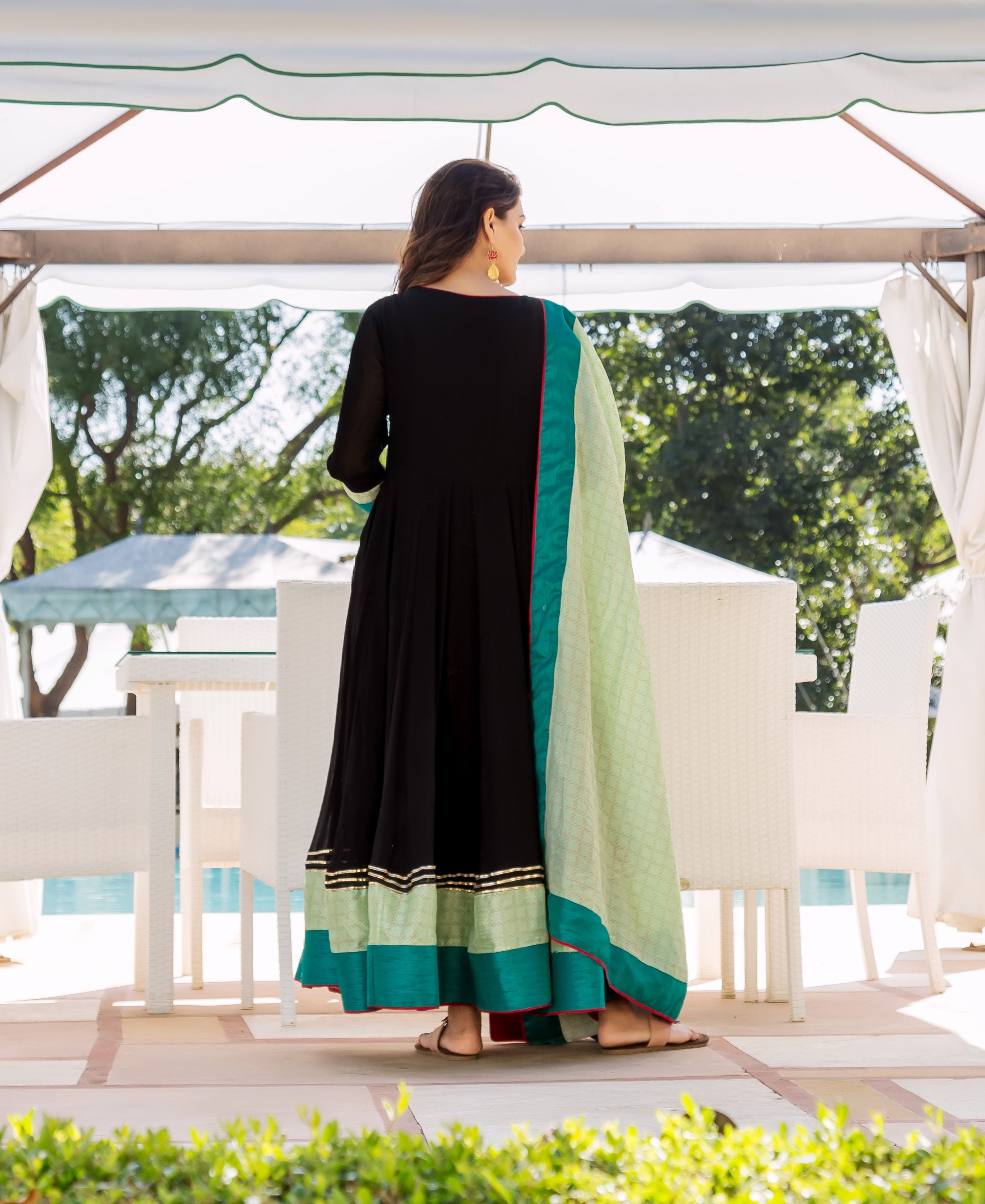 A woman in a black and lime green Anarkali dress with gold accents, facing away.