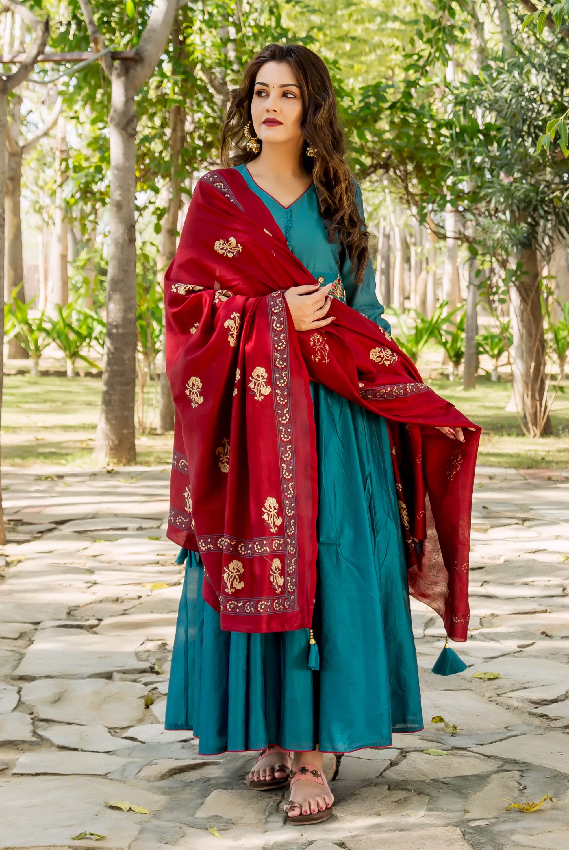 Woman wearing teal anarkali dress with red and gold dupatta and gold hoop earrings.