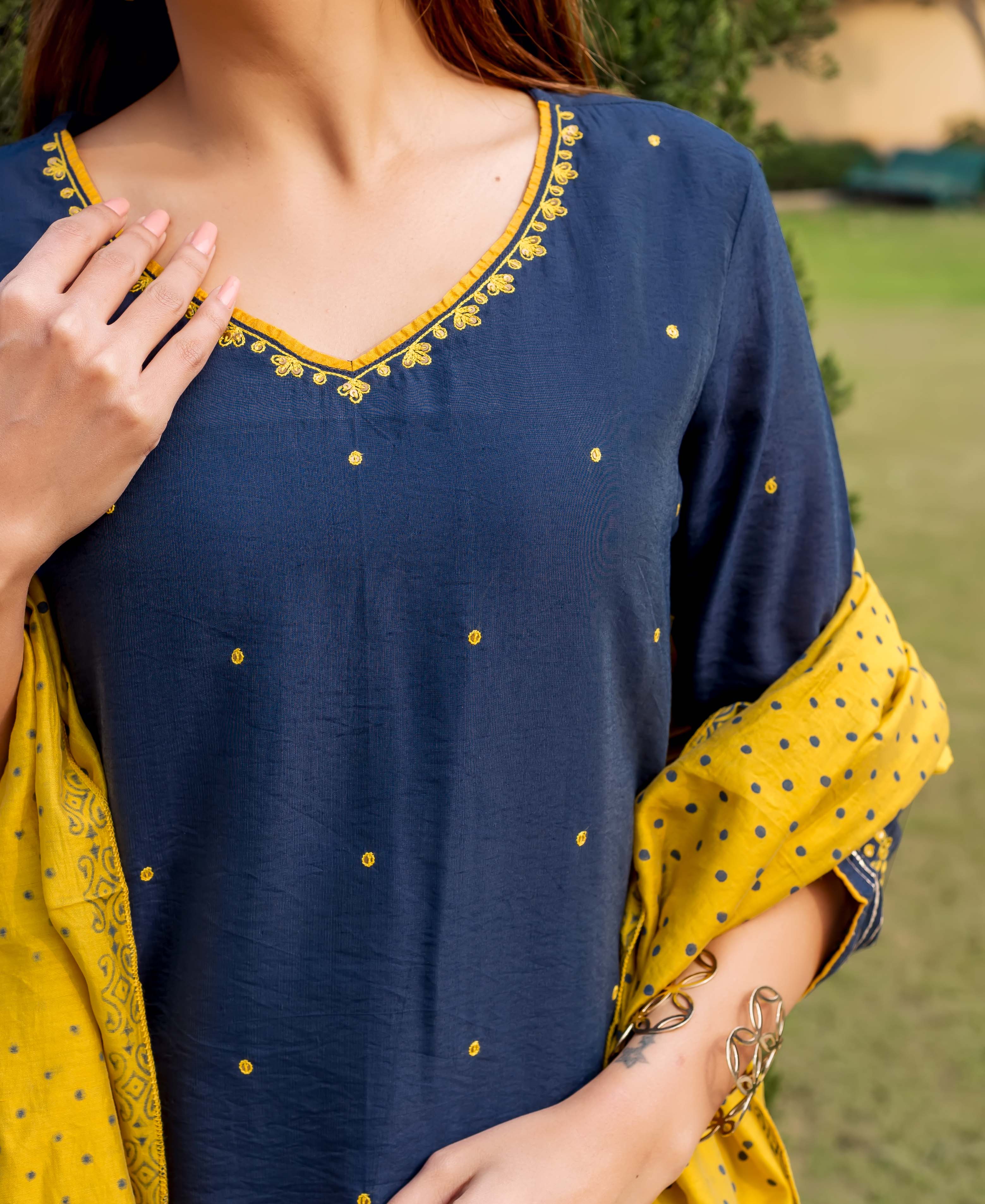 Model in navy blue kurta with yellow embroidered V-neck, dots, and yellow polka dot dupatta.