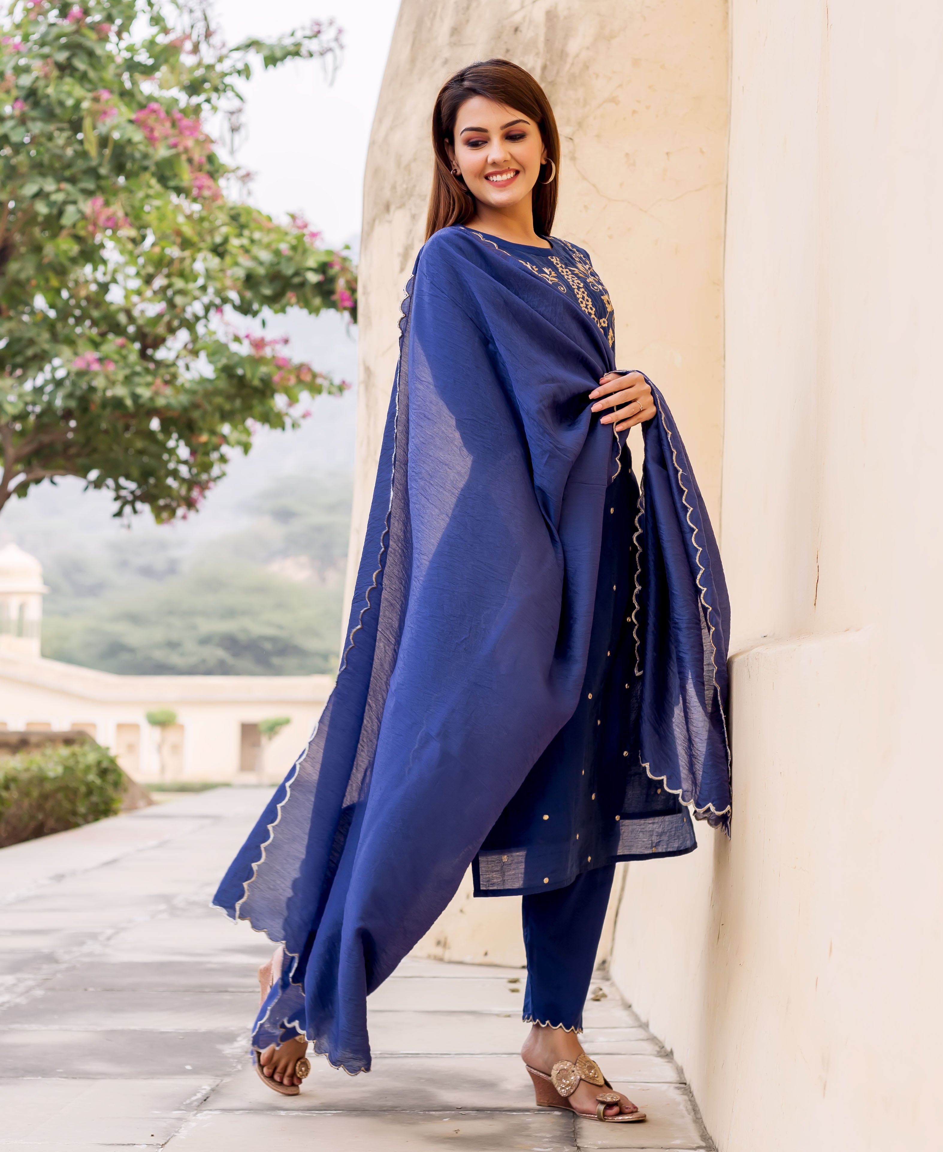 Smiling model wears a midnight blue hand-embroidered kurta set with gold scalloped trim.