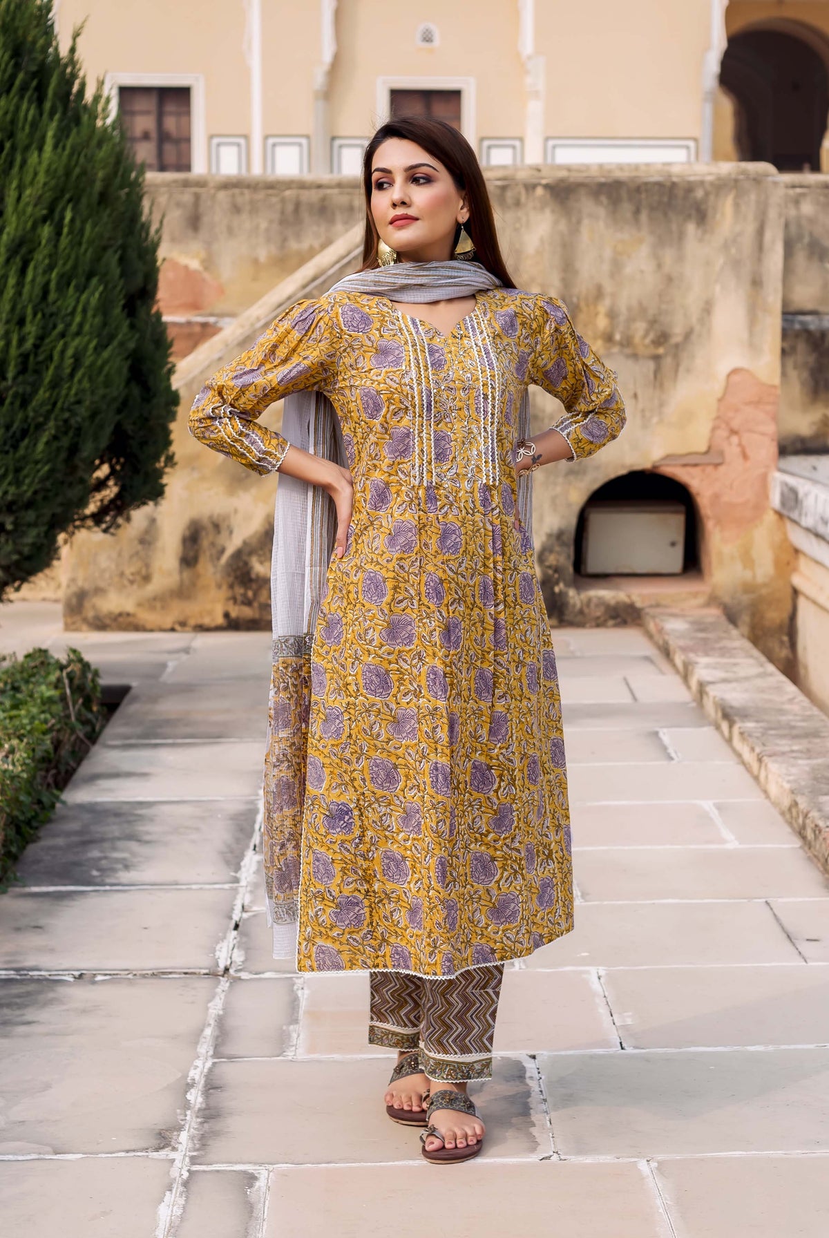 Model in yellow kurta with purple floral block print, grey dupatta, and patterned pants.