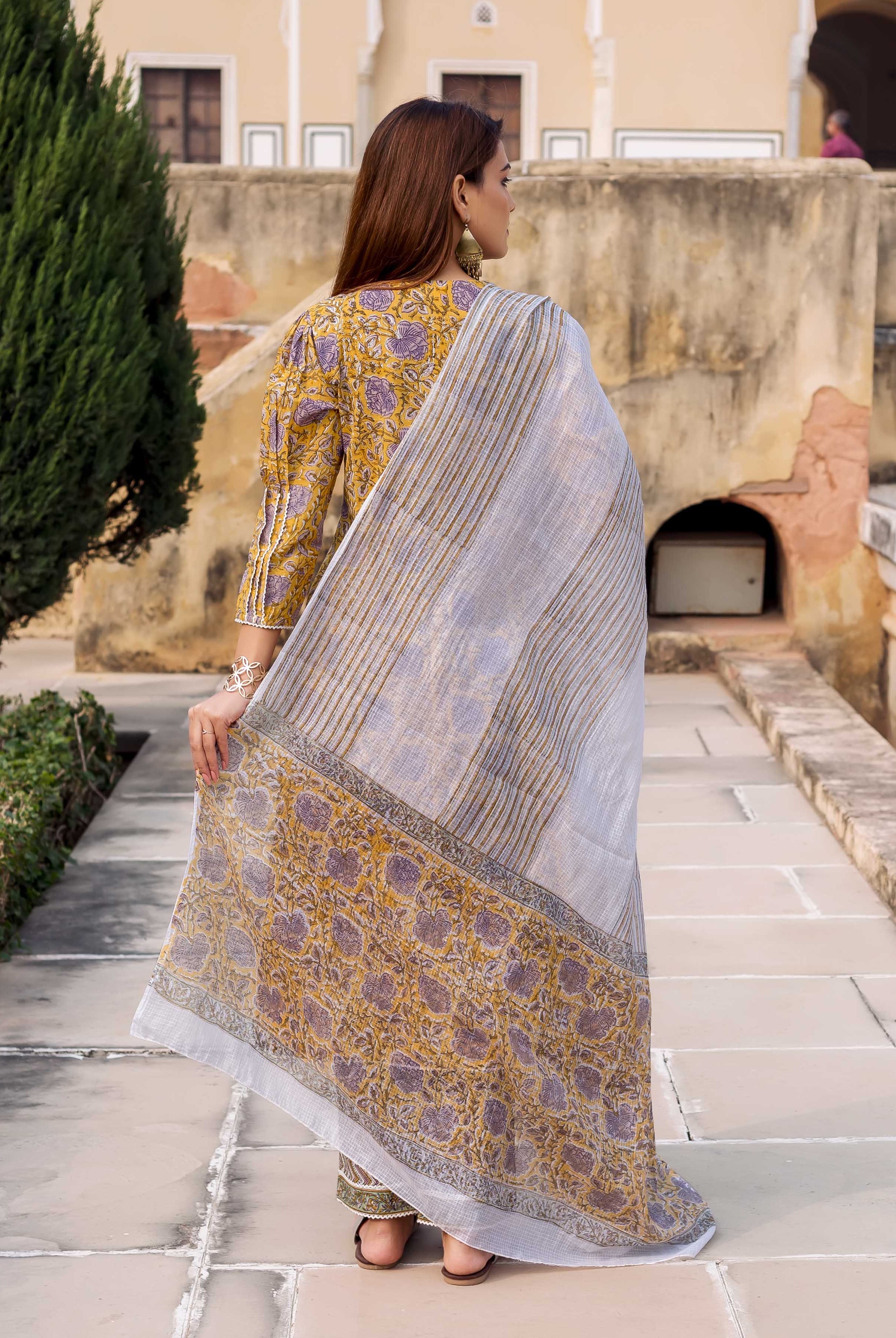 Rear view model in yellow floral block-printed straight kurta with grey striped dupatta.