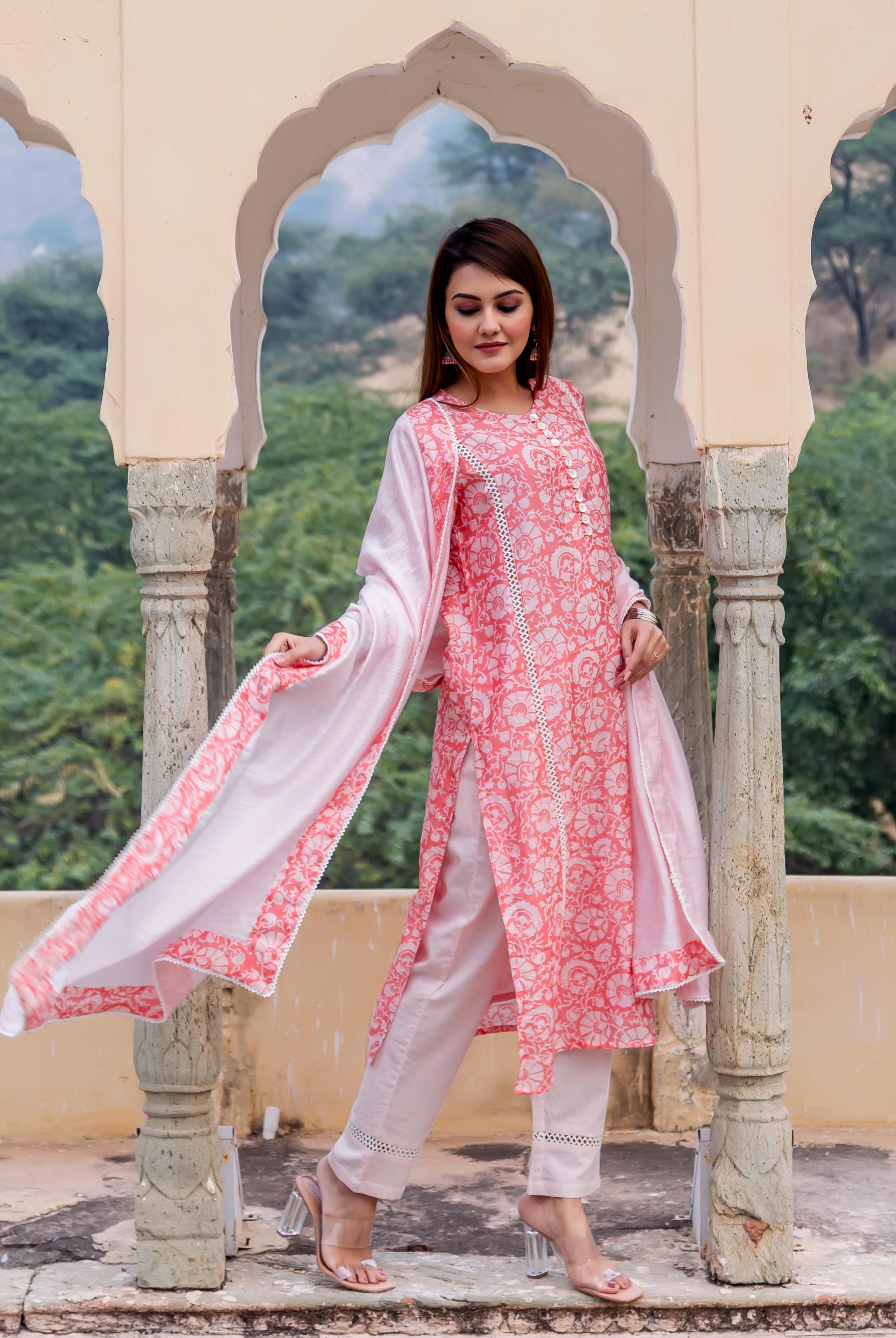 Woman wears a peach hand block printed kurta set with white pants and flowing dupatta.
