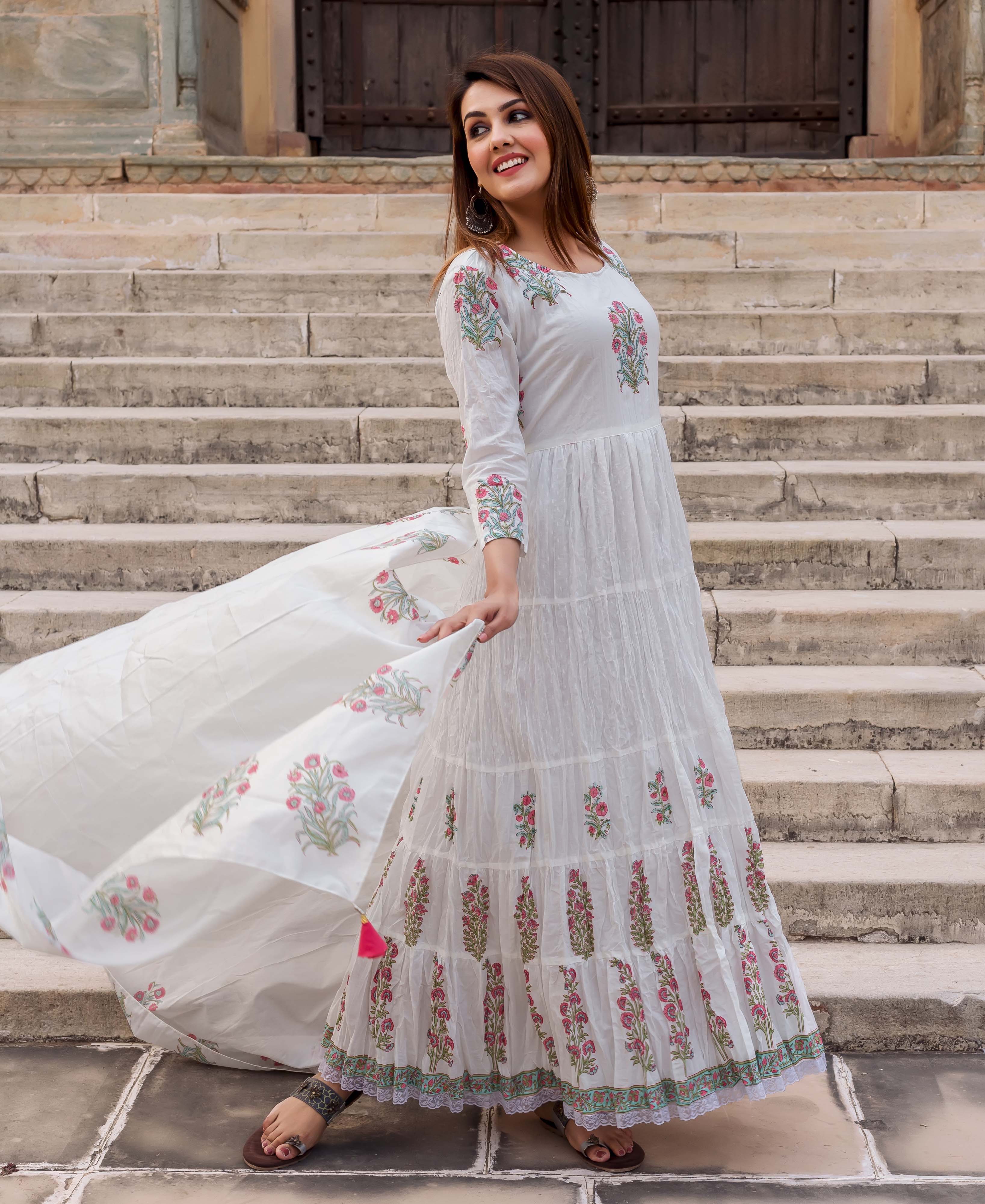 Woman in white tiered dress with pink and green floral butta print and flowing dupatta.