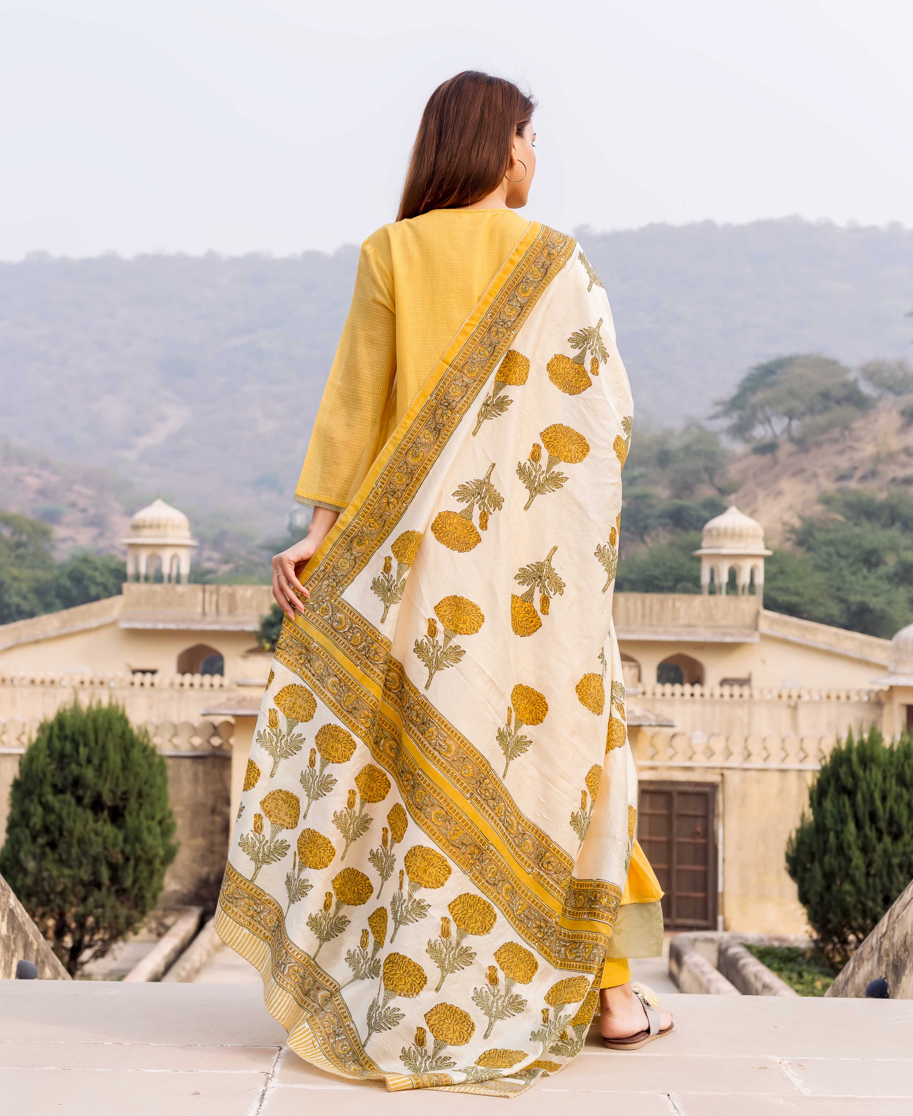 Rear view of model in honey yellow kurta and white hand-block printed floral dupatta.